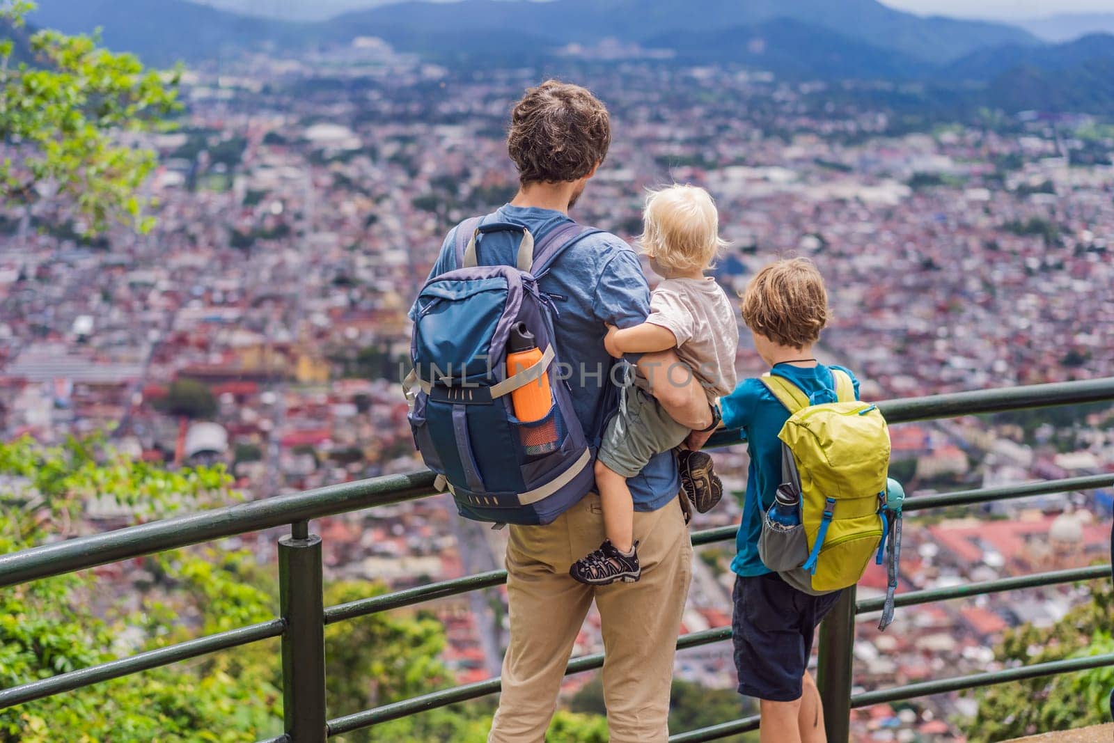 Dad and her two sons, a baby and a teenager tourists in front of the panoramic view of Orizaba from Cerro del Borrego, Mexico. Travel, scenic landscape, and adventure concept.
