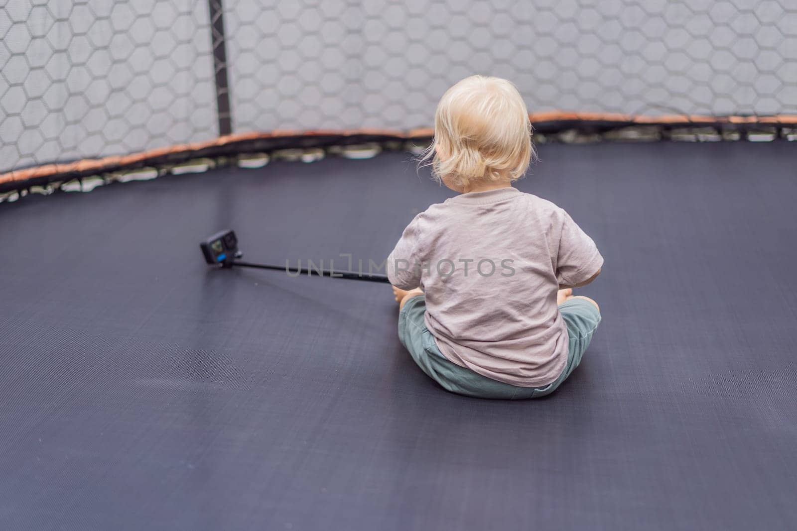 Toddler sitting on a trampoline with an action camera. Childhood adventure, exploration, and playful moments concept.