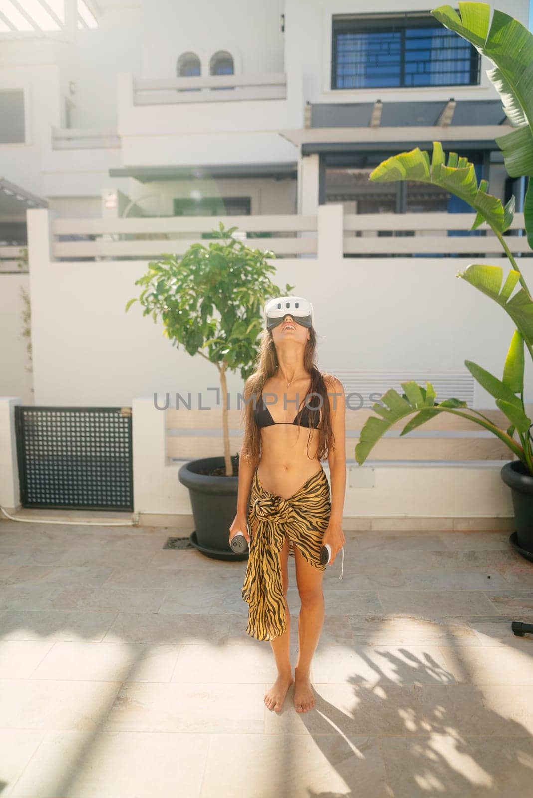 A young woman in a stylish bikini stands confidently in a vibrant outdoor space surrounded by lush greenery