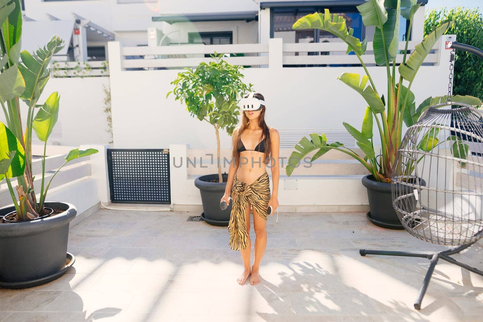 A stylish young woman in a bikini and sarong enjoys a sunny day happily using a virtual reality headset