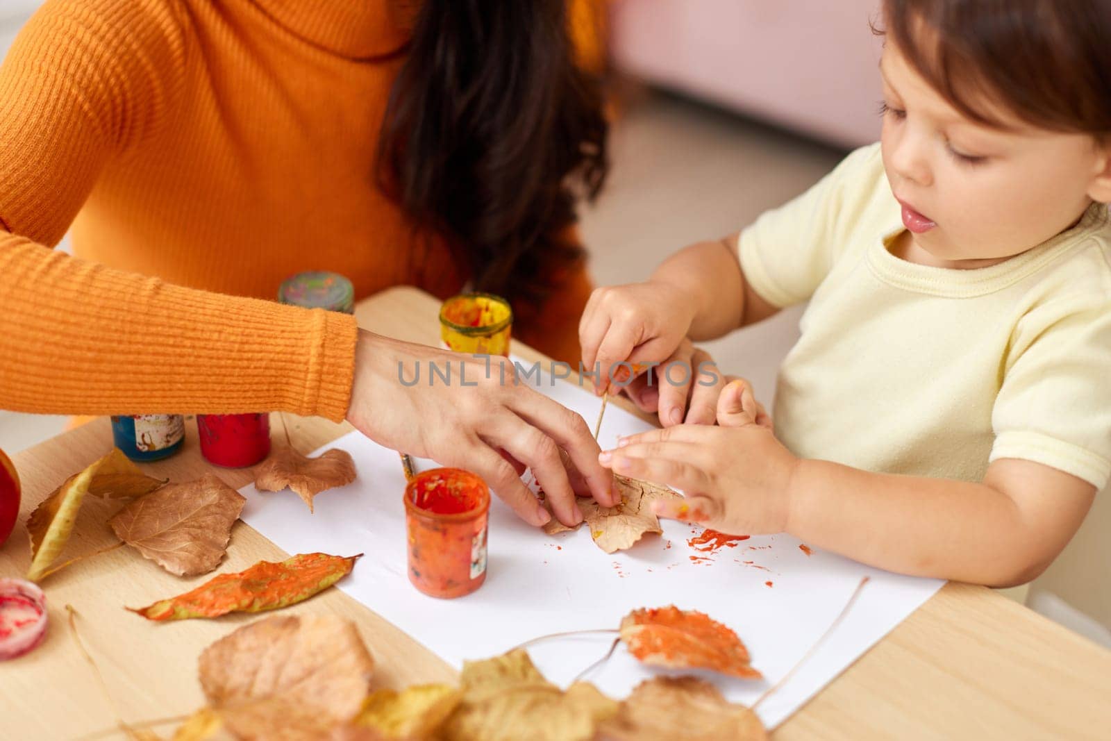 close-up, child and mom hands painting autumn yellow leaves together. happy time together at home