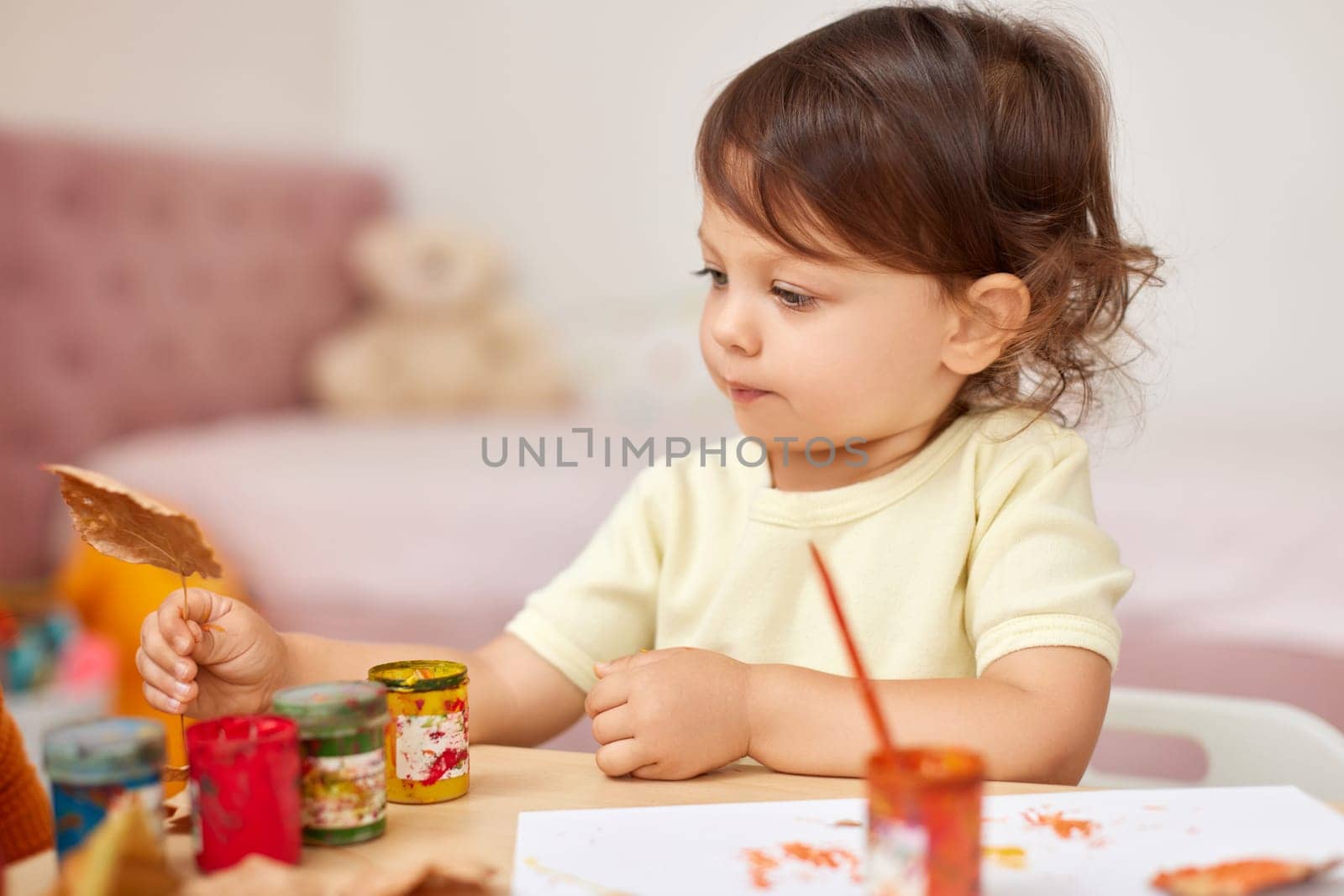 happy little child girl painting autumn leaves. baby girl drawing leaves in yellow and orange paint