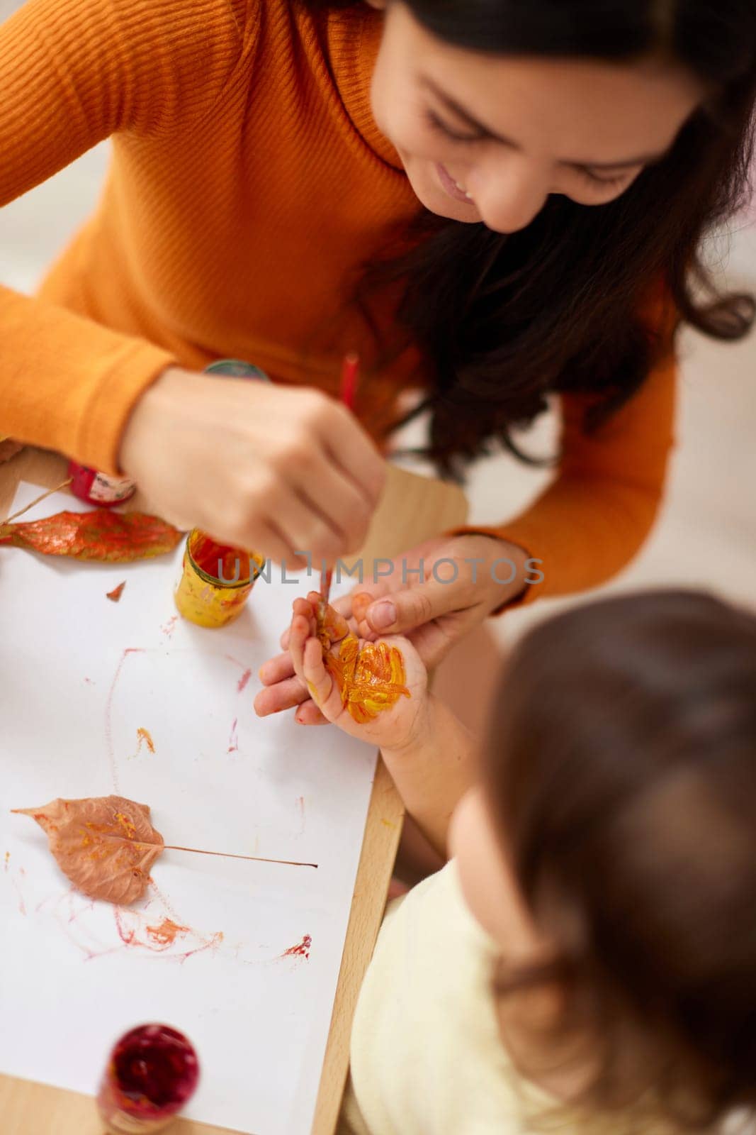 Cute little girl and mom spending good time painting hands and autumn yellow leaves together