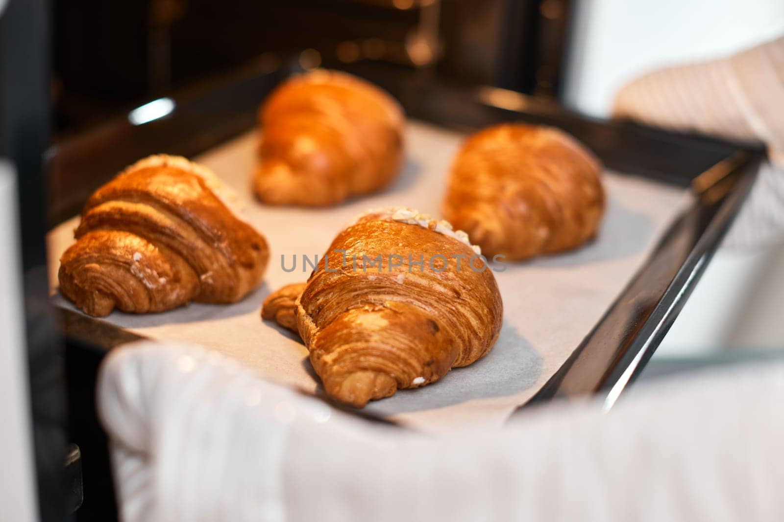 female baker taking tray with fresh croissants from oven in modern kitchen, close-up