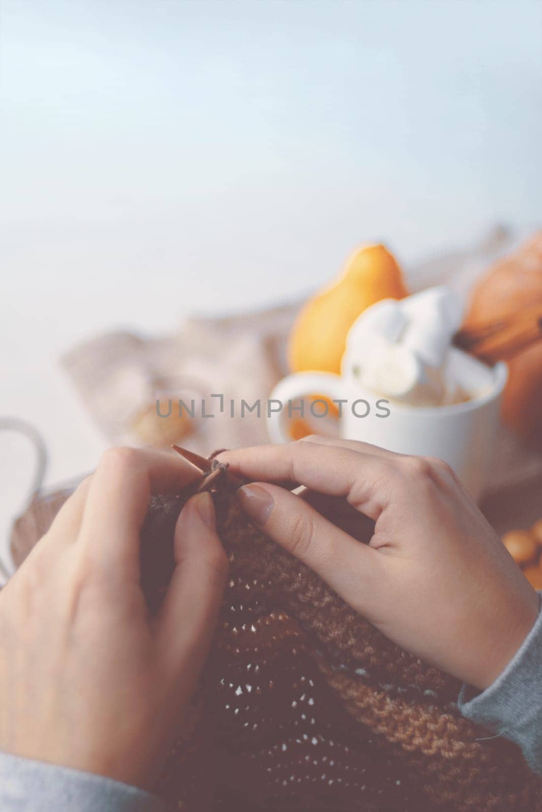 Hands knitting wool with a cozy drink and pastries in the background, perfect for a relaxing hobby time.