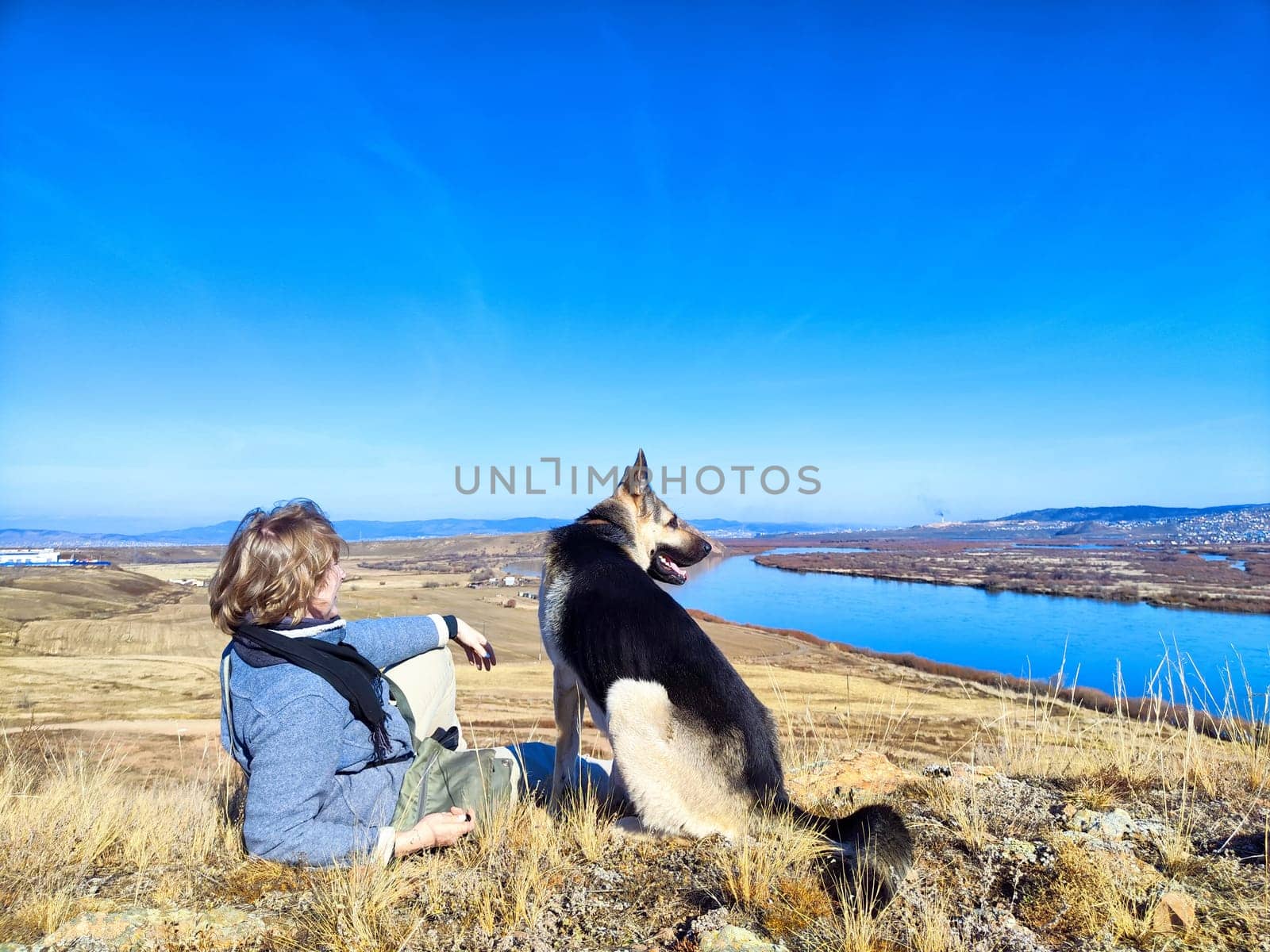 A woman and her German Shepherd enjoy a hike overlooking a picturesque lake on a clear sunny spring morning