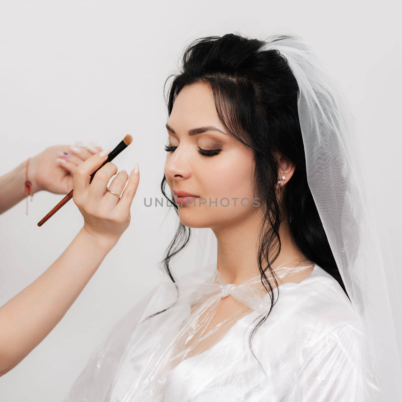 make-up artist hands with a brush makes up and apply shadows on the eyes of the bride's girl in the beauty salon