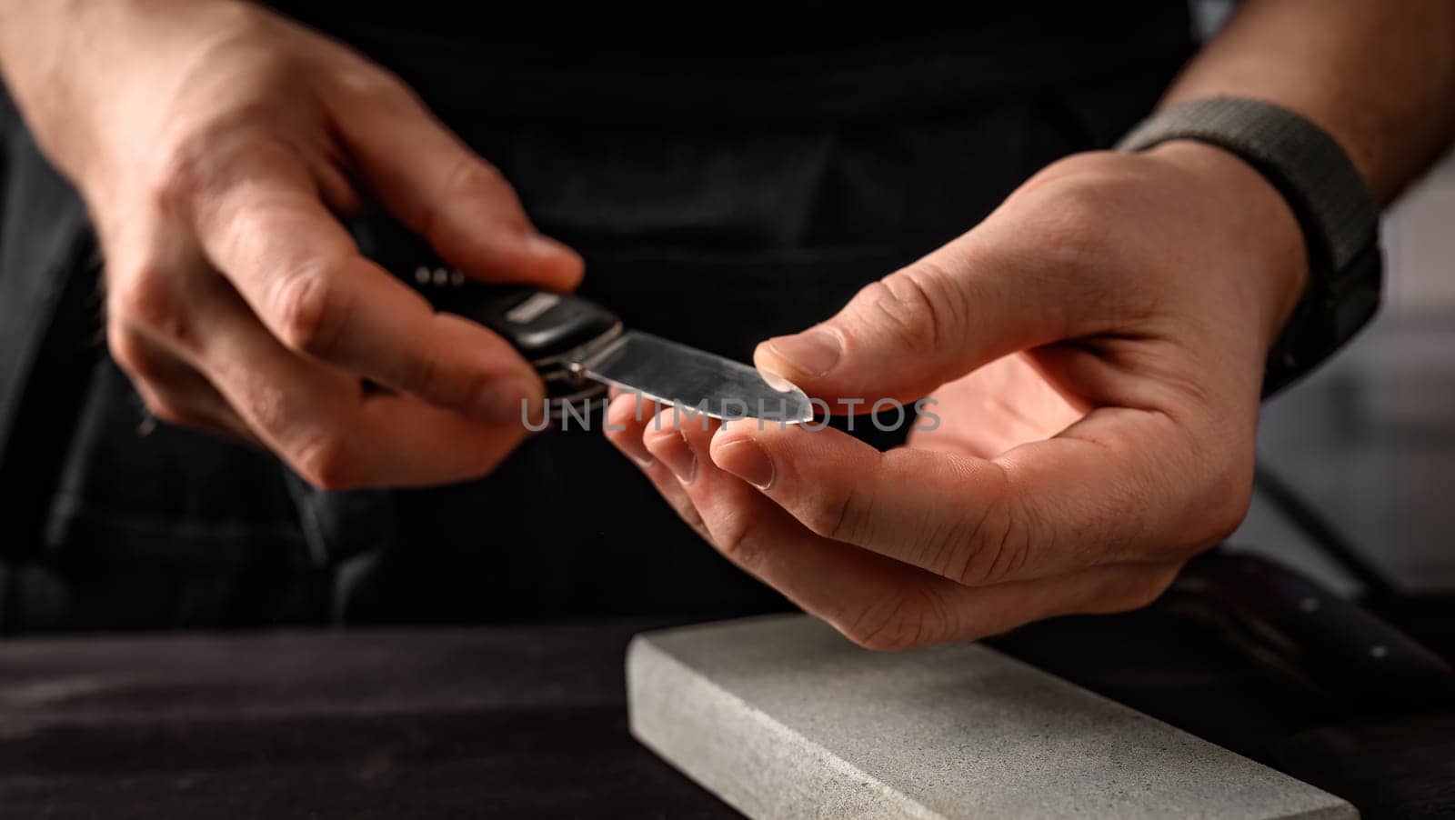 Man's hands with folding knife and sharpen stone tool. master sharpening penknife on a grindstone