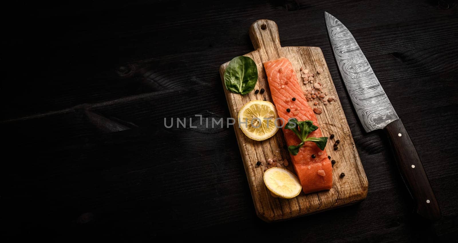 Raw red fish salmon fillet with herbs and lemon on a cutting board ready for cooking healthy dinner, top view with copy space