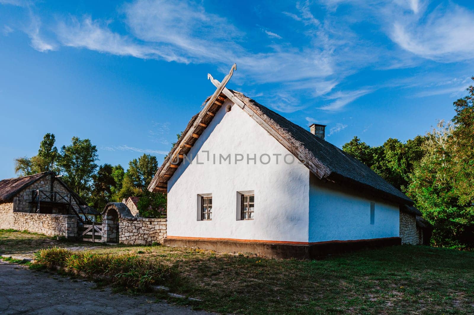 Charming rural house with a traditional thatched roof stands in a peaceful countryside setting under a bright blue sky.