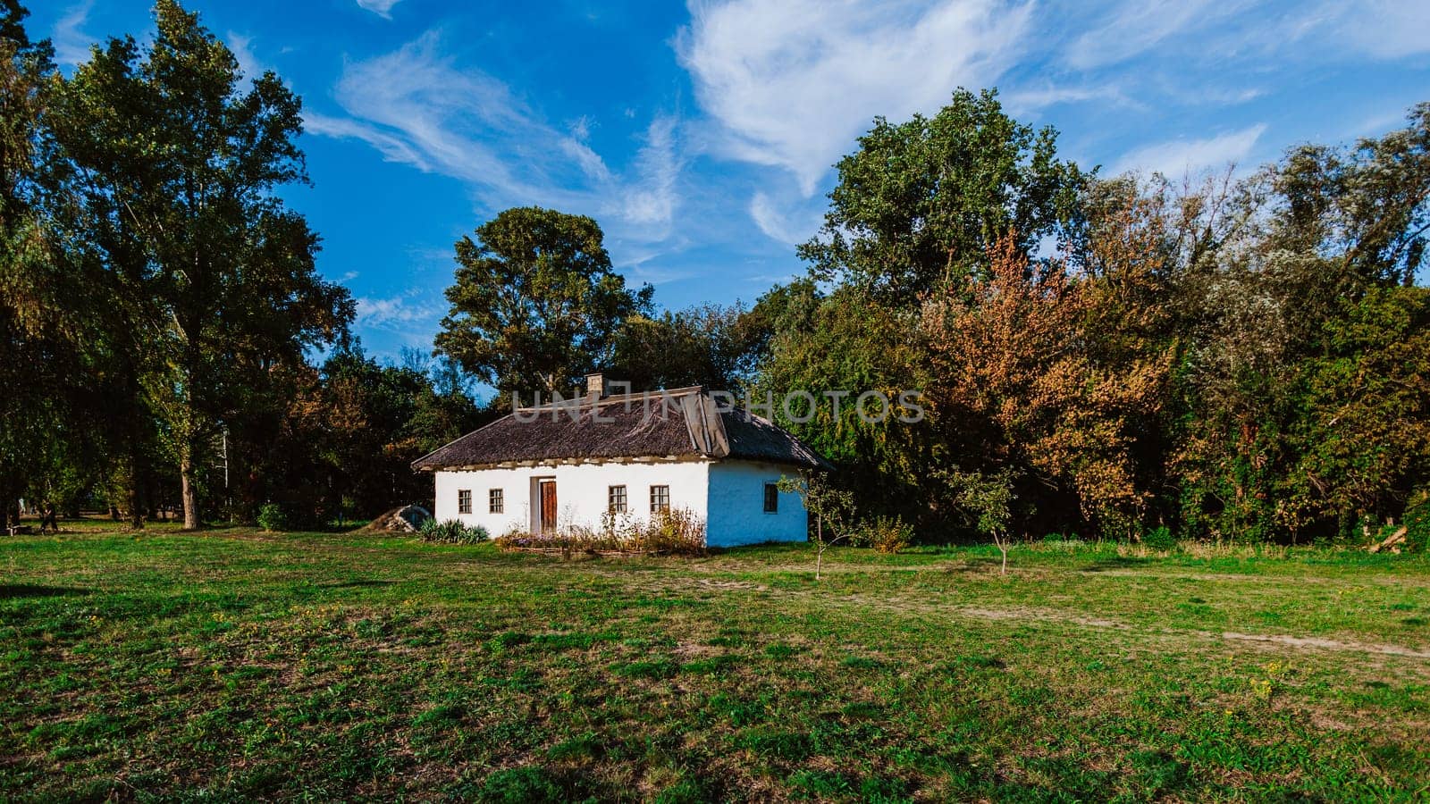 Traditional rural house with a thatched roof is nestled in a peaceful countryside surrounded by trees and greenery.
