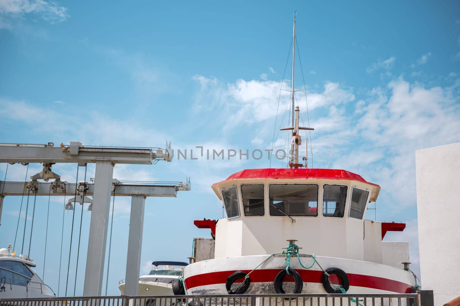 A vibrant red and white boat docked on land, undergoing maintenance. The clear blue sky and the ship's equipment create a nautical scene.