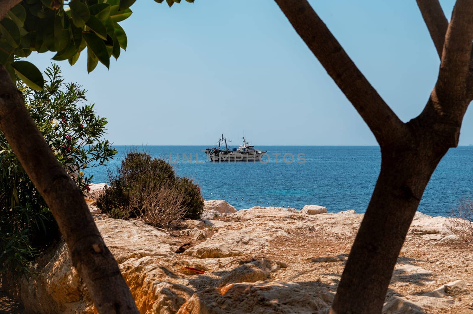 A serene seascape with a boat floating on calm blue waters, framed by rocky coastline and lush greenery, evoking peace and exploration.