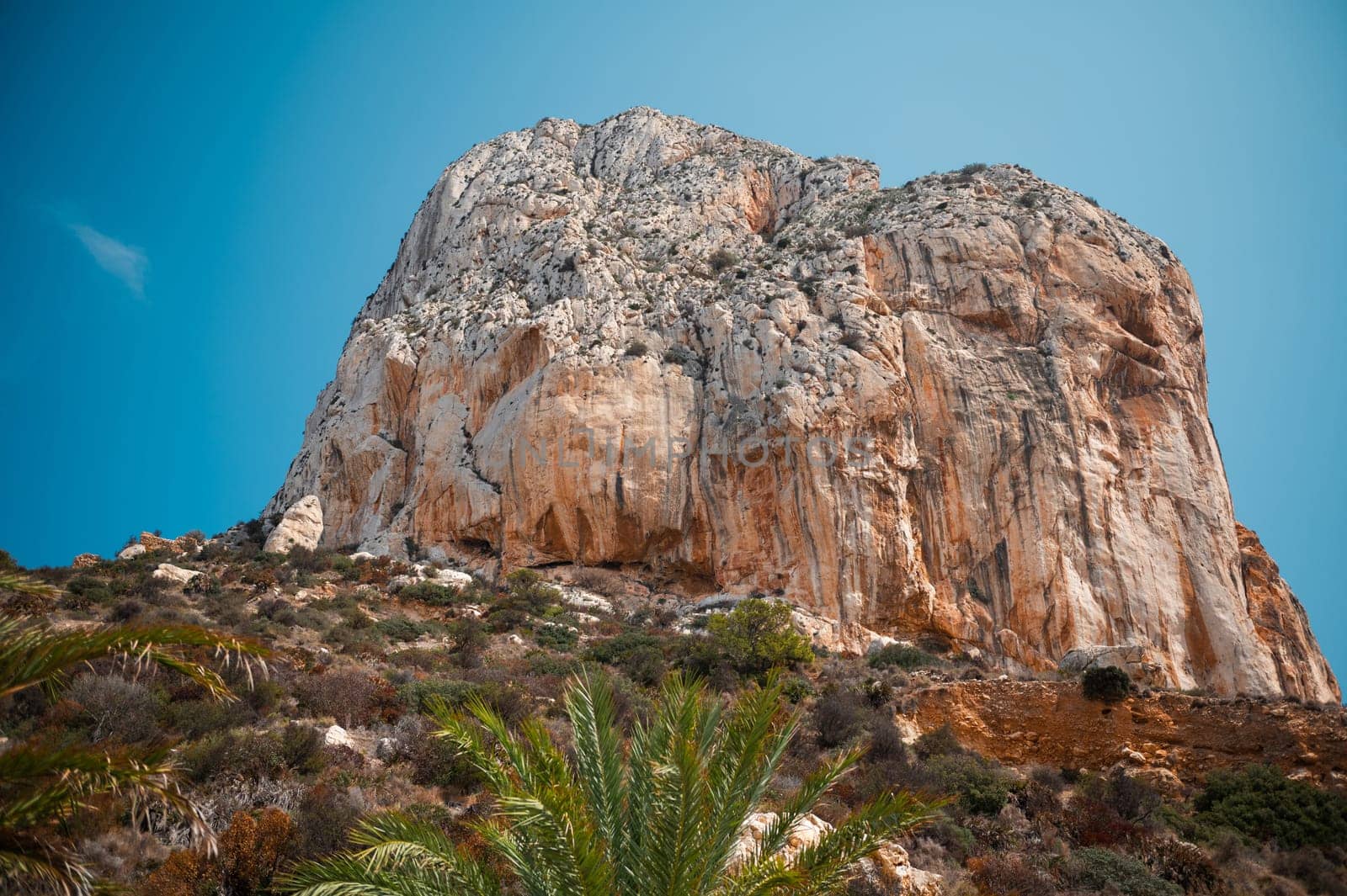 A stunning rocky cliff rises against a vibrant blue sky, surrounded by lush vegetation. The scene evokes feelings of adventure and serenity, capturing the beauty of nature.