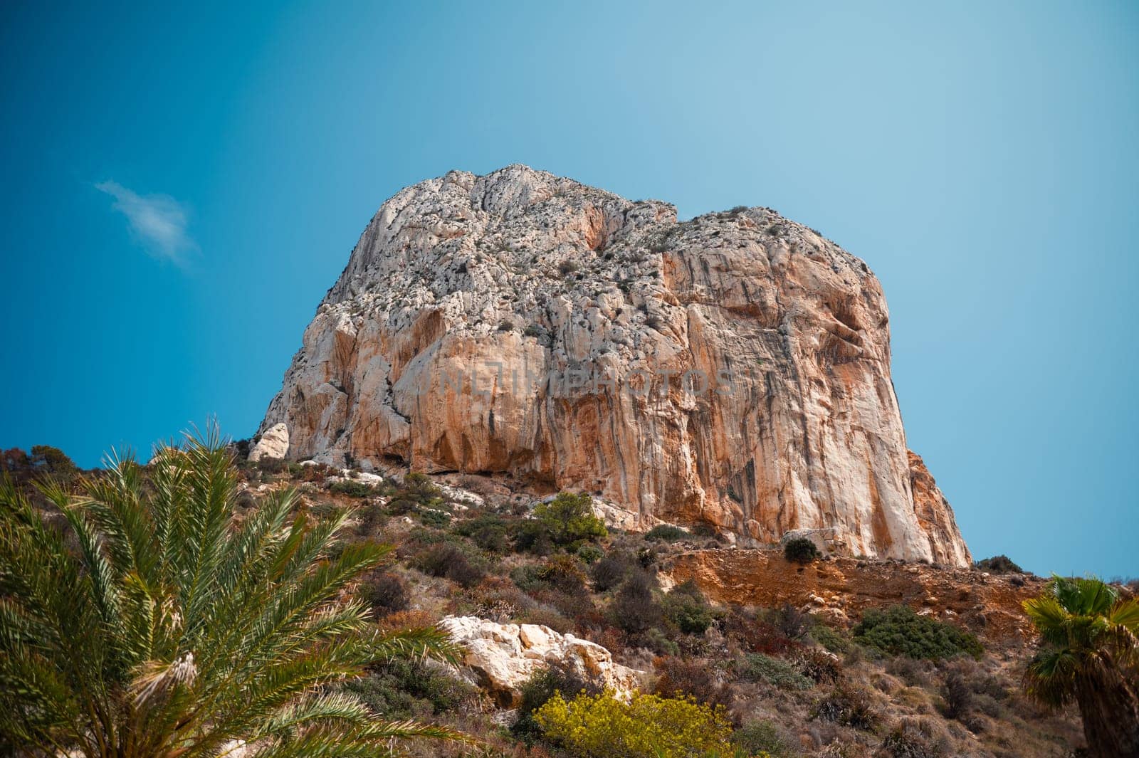A stunning view of a towering rocky cliff under a clear blue sky, surrounded by lush green vegetation, representing nature's beauty and serenity.