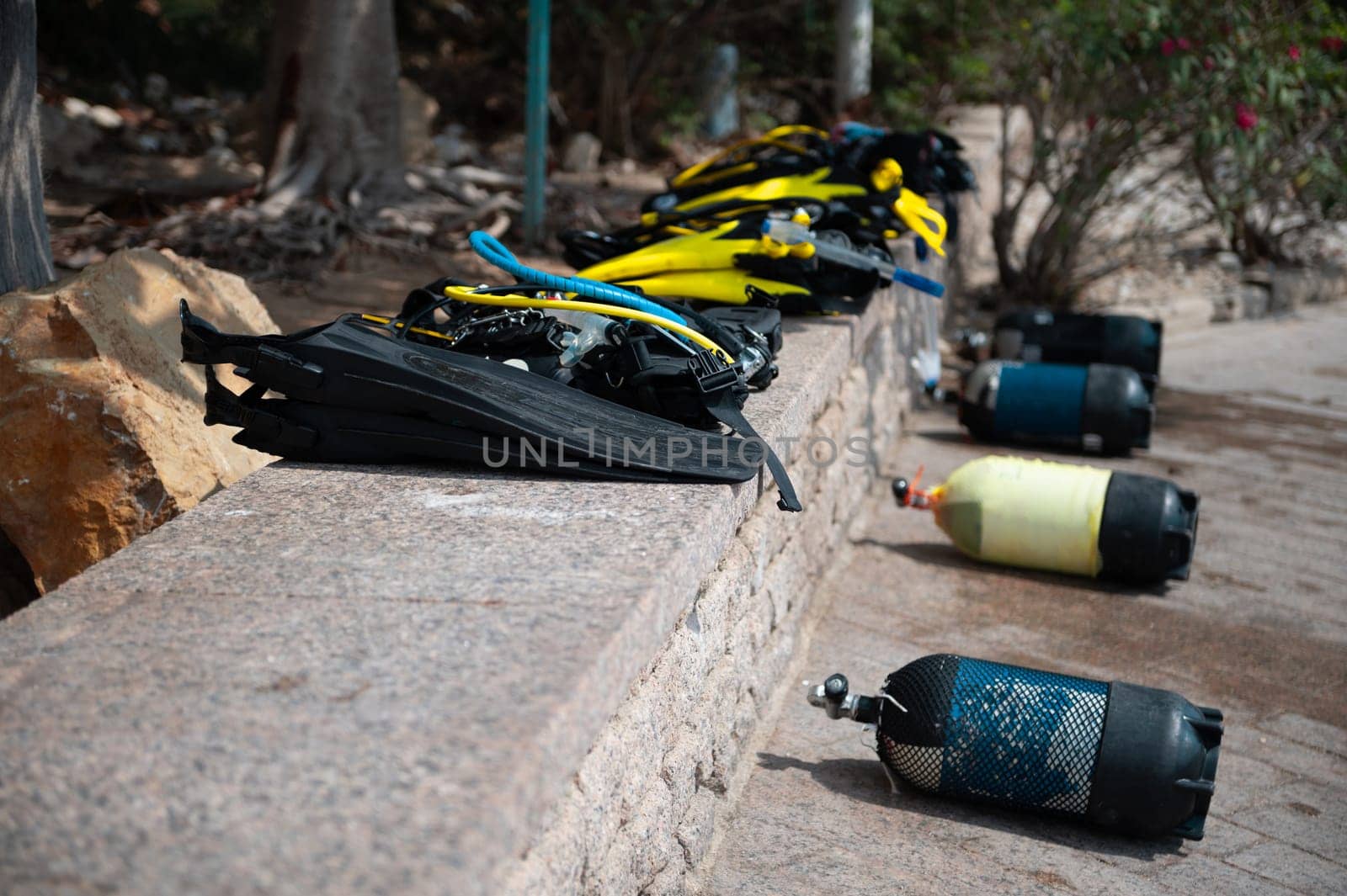 Scuba diving equipment including fins, tanks, and masks neatly organized on a stone wall near the beach, ready for an underwater adventure.