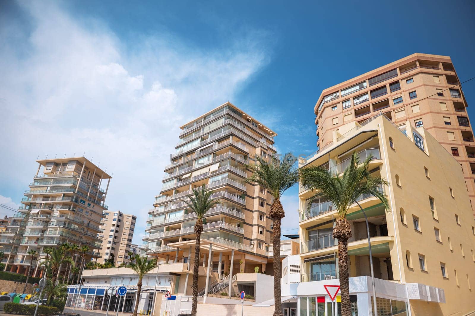 View of modern apartment buildings against a clear blue sky, surrounded by palm trees, creating a sunny and tropical atmosphere.