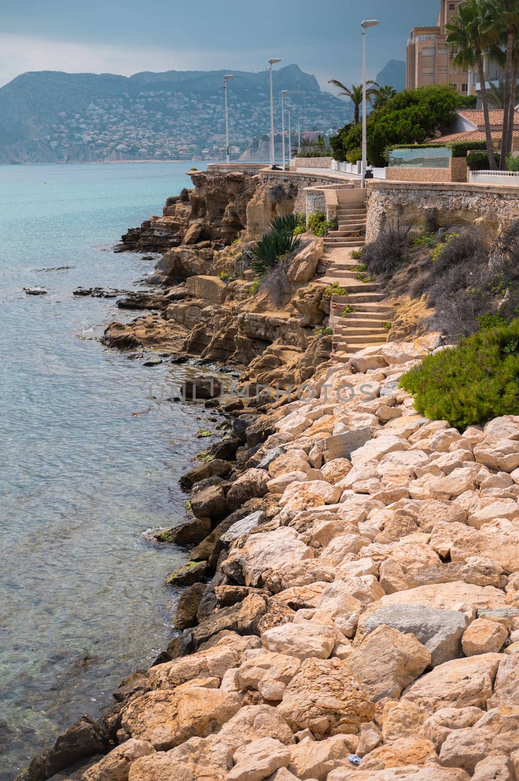 A scenic coastal pathway flanked by rocky shores with a view of the ocean, under cloudy skies, located in a serene seaside setting.