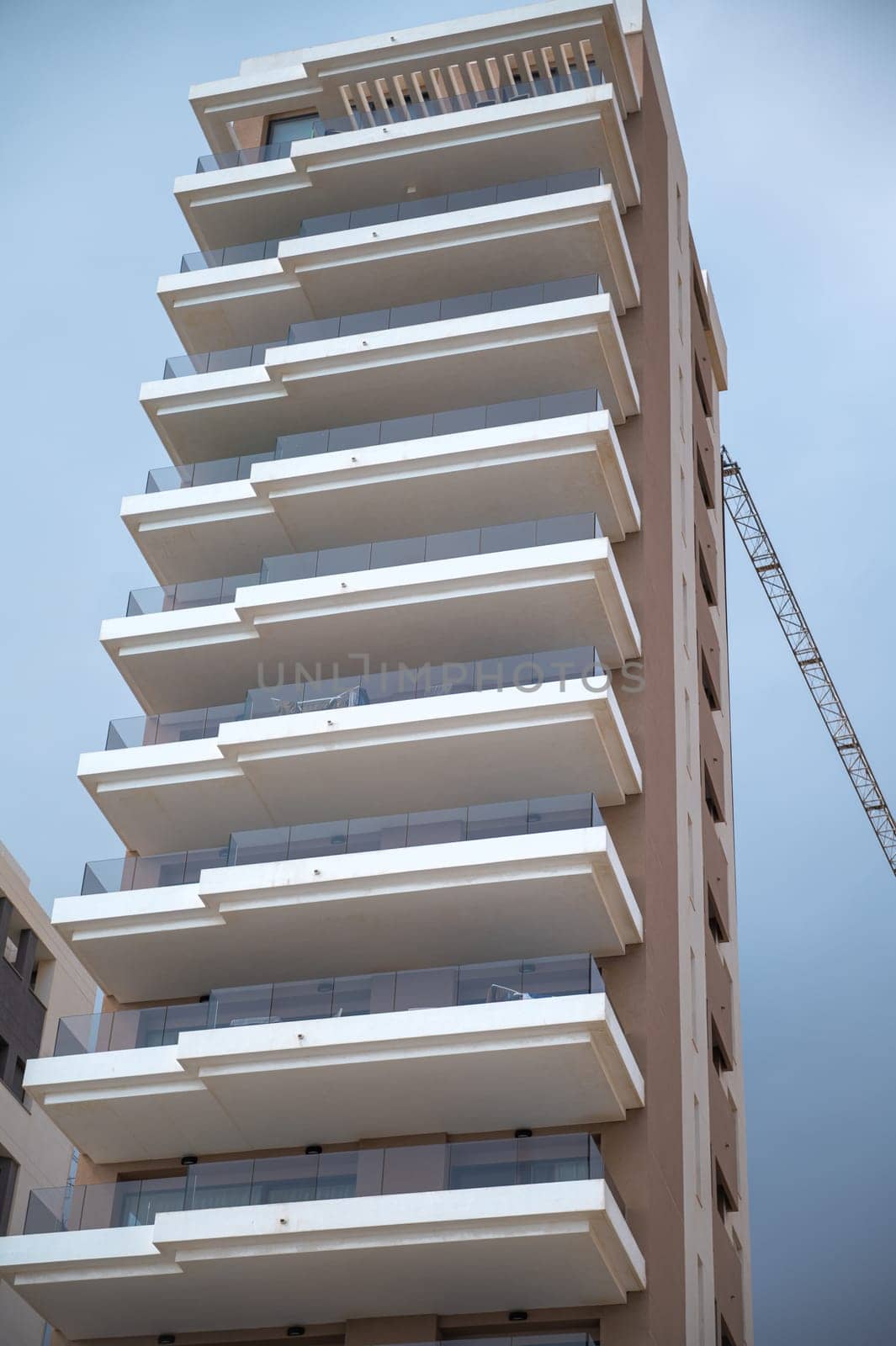 Contemporary multi-story building featuring sleek glass balconies and a construction crane, set against a clear sky.