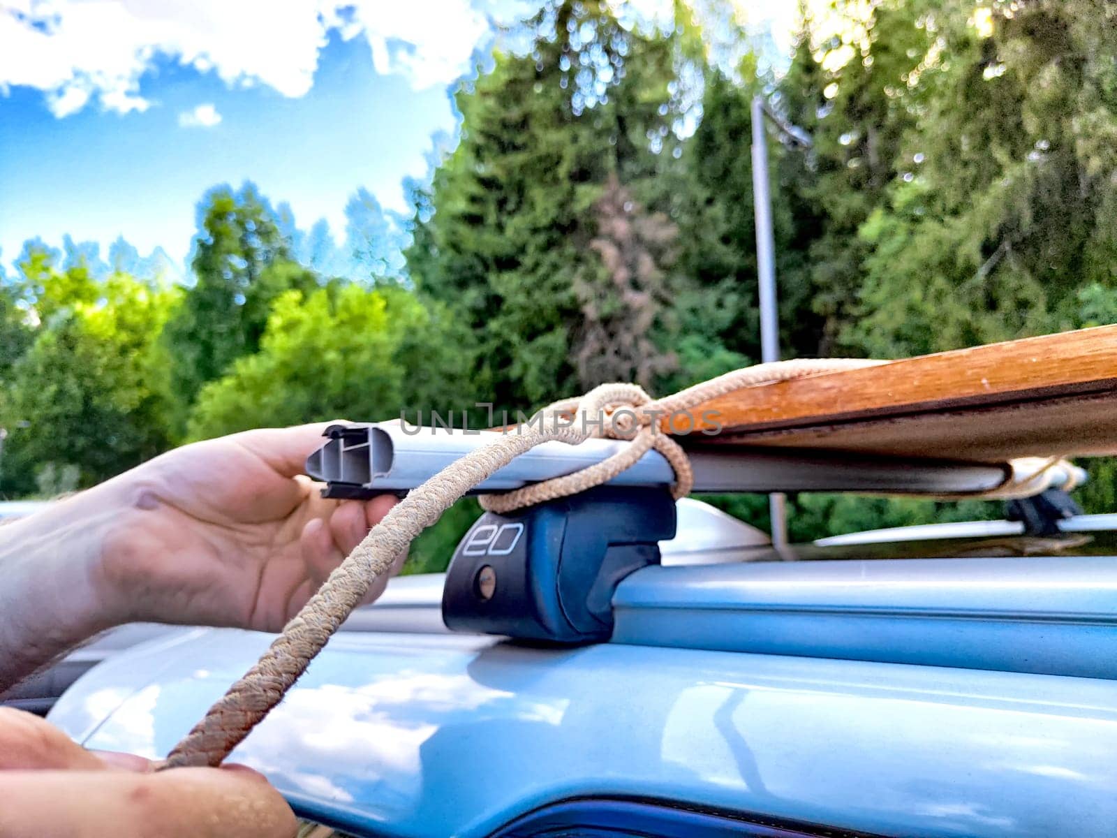A hand secures wooden planks to a vehicle roof, ideal for travel, adventures, and outdoor activities