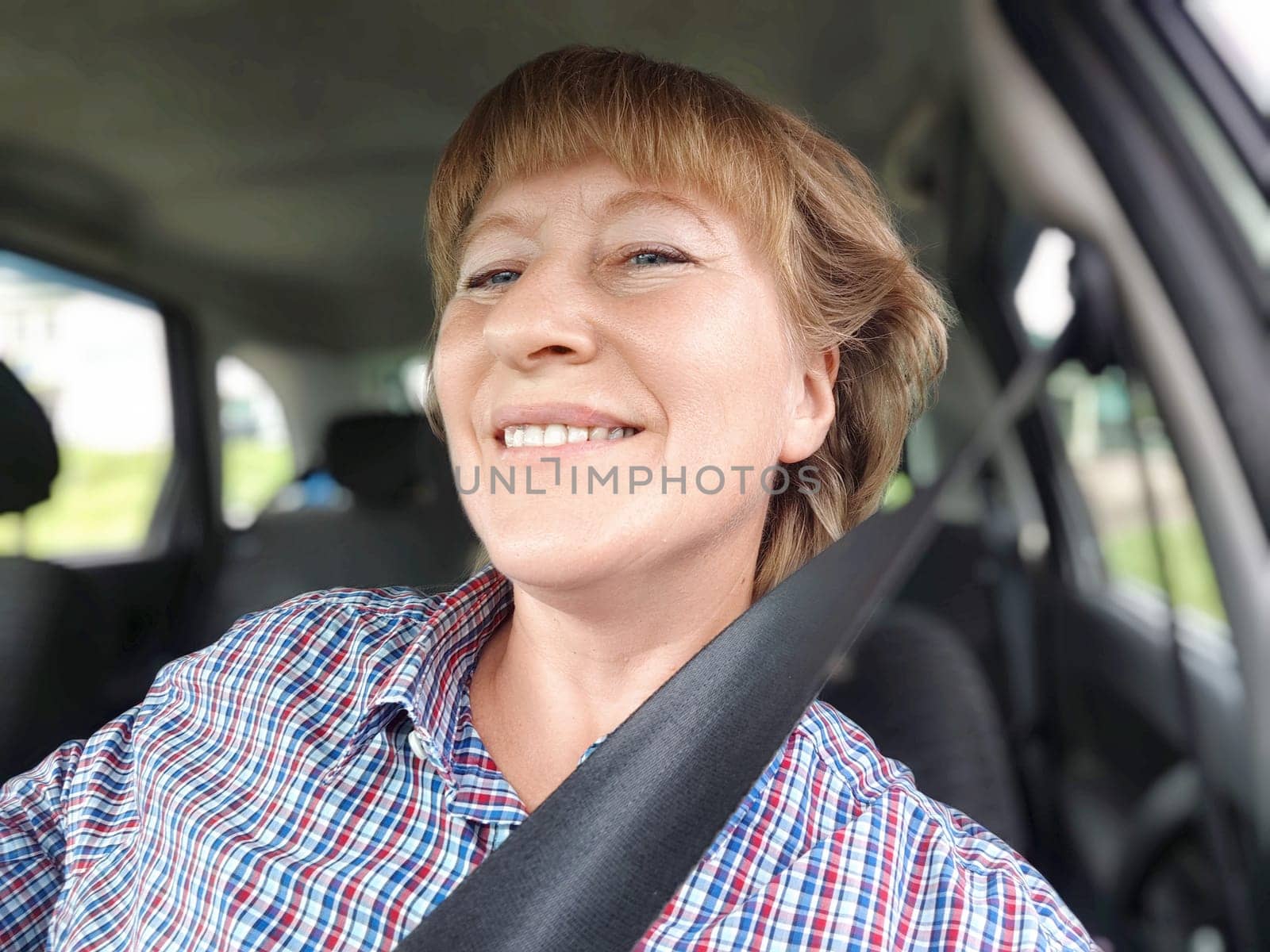 Middle aged woman is seated in a car, smiling cheerfully as she securely fastens her seat belt. Safety in transport. Traffic Laws