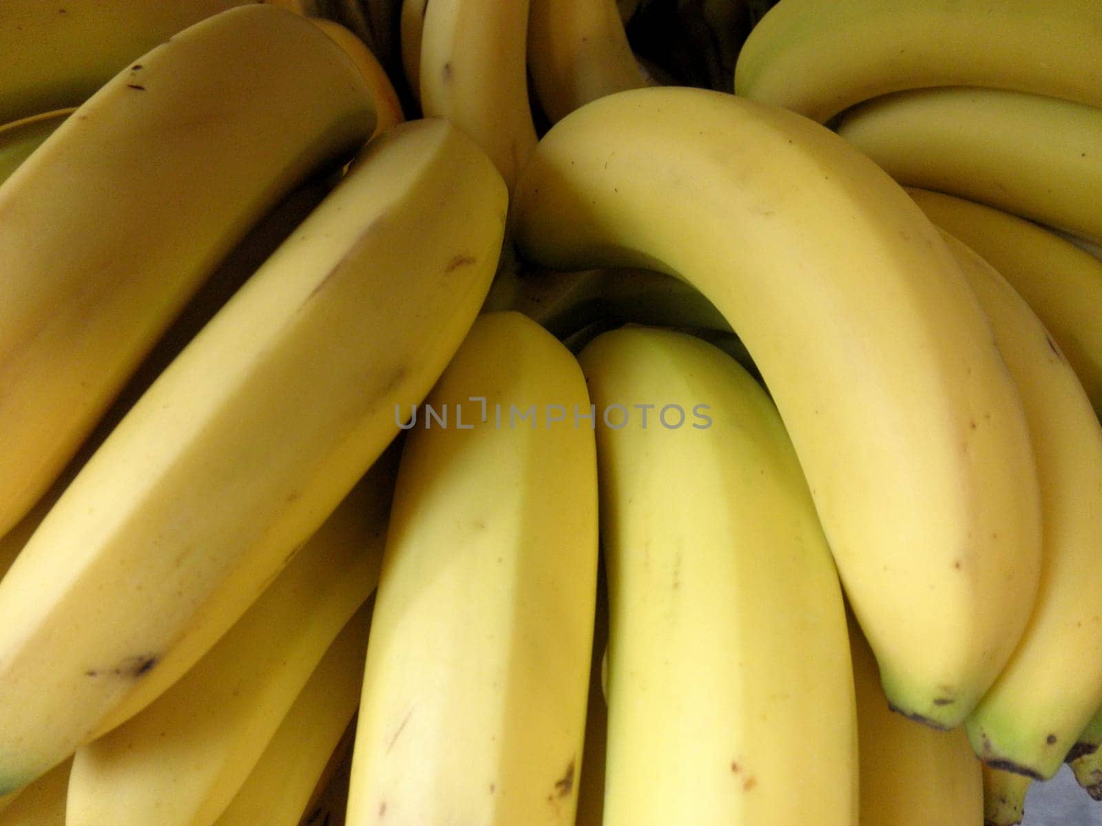 A fresh bunch of ripe bananas fills the view, showcasing their bright yellow skin and smooth texture, ready for purchase at the local market.