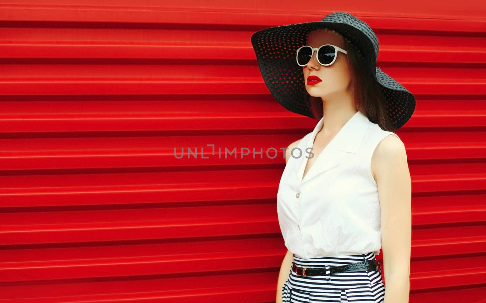 Portrait of stylish young woman model posing wearing black summer straw round hat on red background
