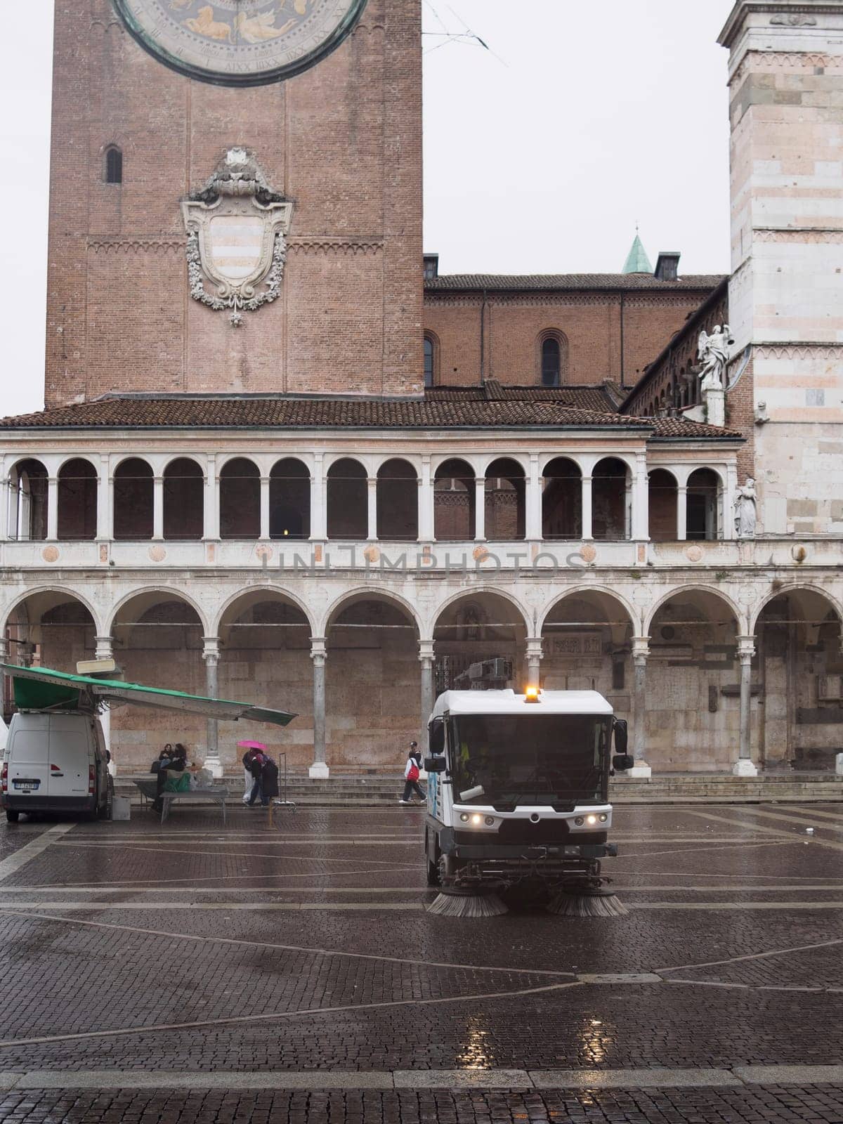Cremona, Italy September 26th 2024 Street sweeper vehicle cleaning the cobblestone square in front of the duomo of cremona, italy, with people walking in the background