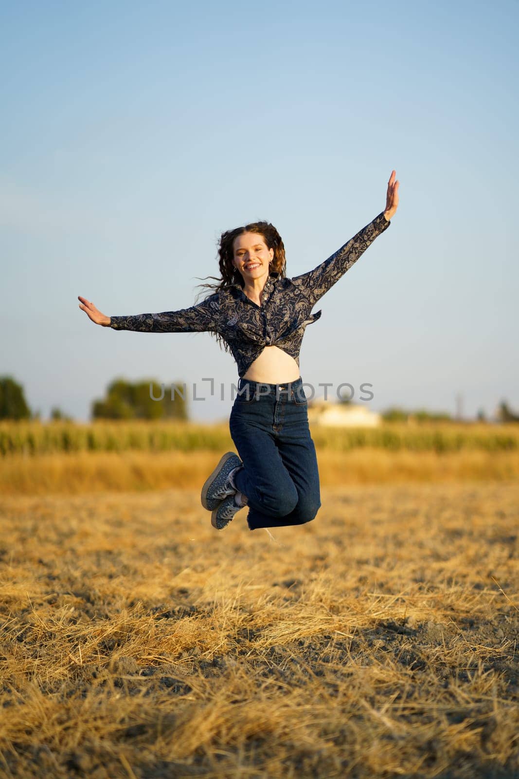 A cheerful and spirited young woman leaps joyfully and exuberantly in a sunlit golden field, embodying the essence of freedom and pure happiness against a serene and picturesque backdrop