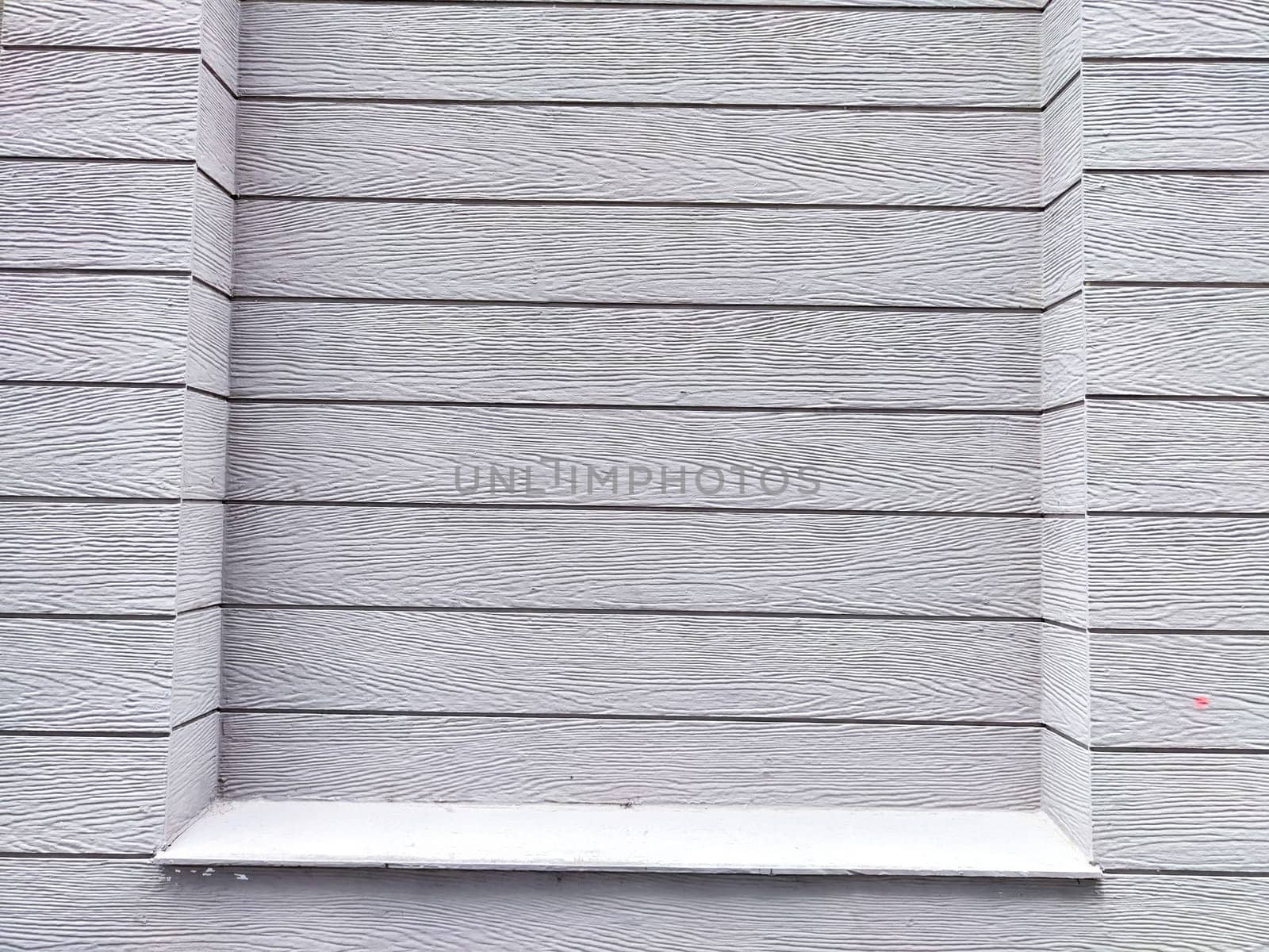 A plain gray wooden wall with distinct textures and a window frame featuring a small ledge.