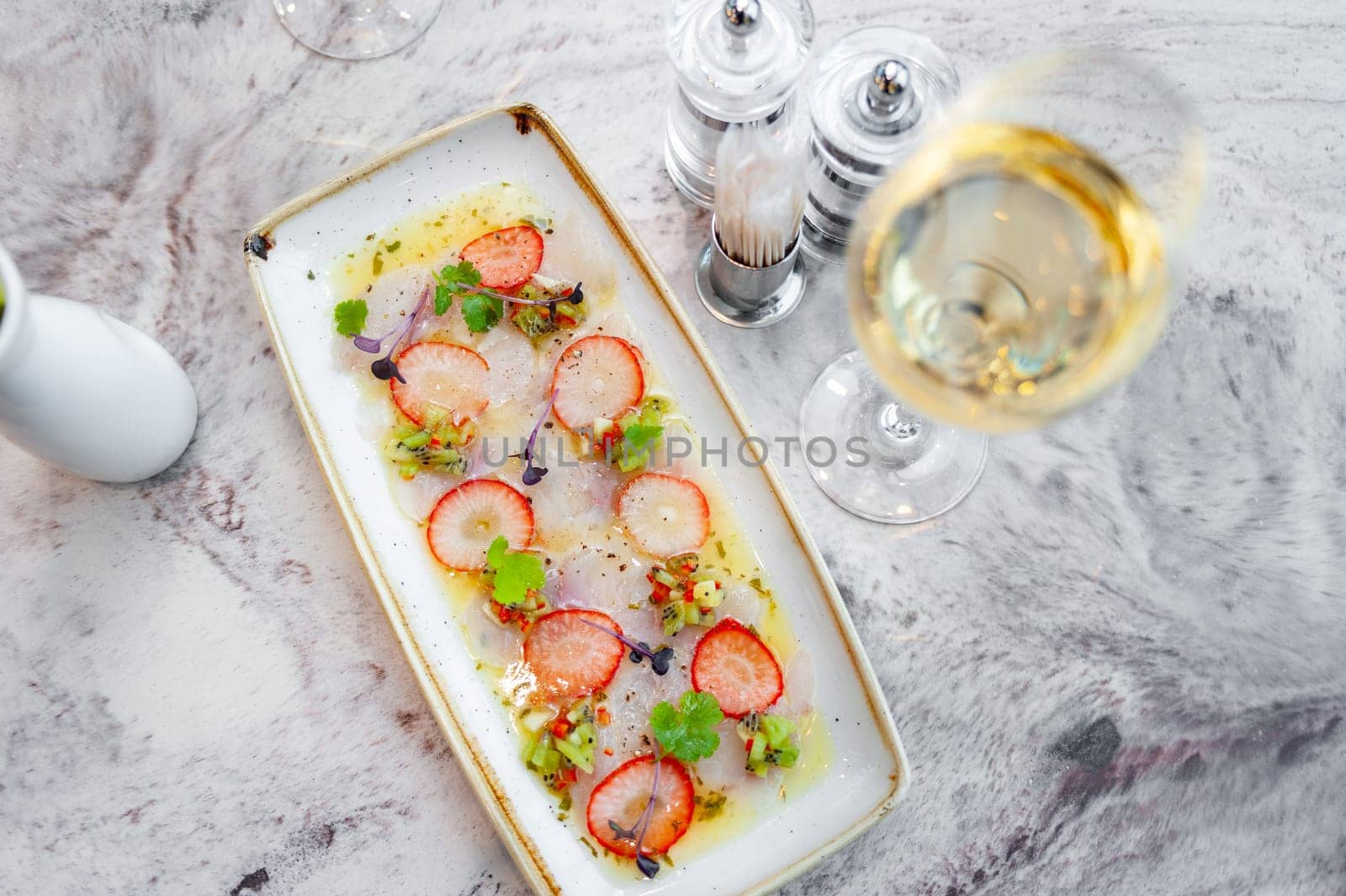 Sea bass ceviche with strawberry, kiwi and mango salsa on a marble table in a restaurant and a glass of white wine