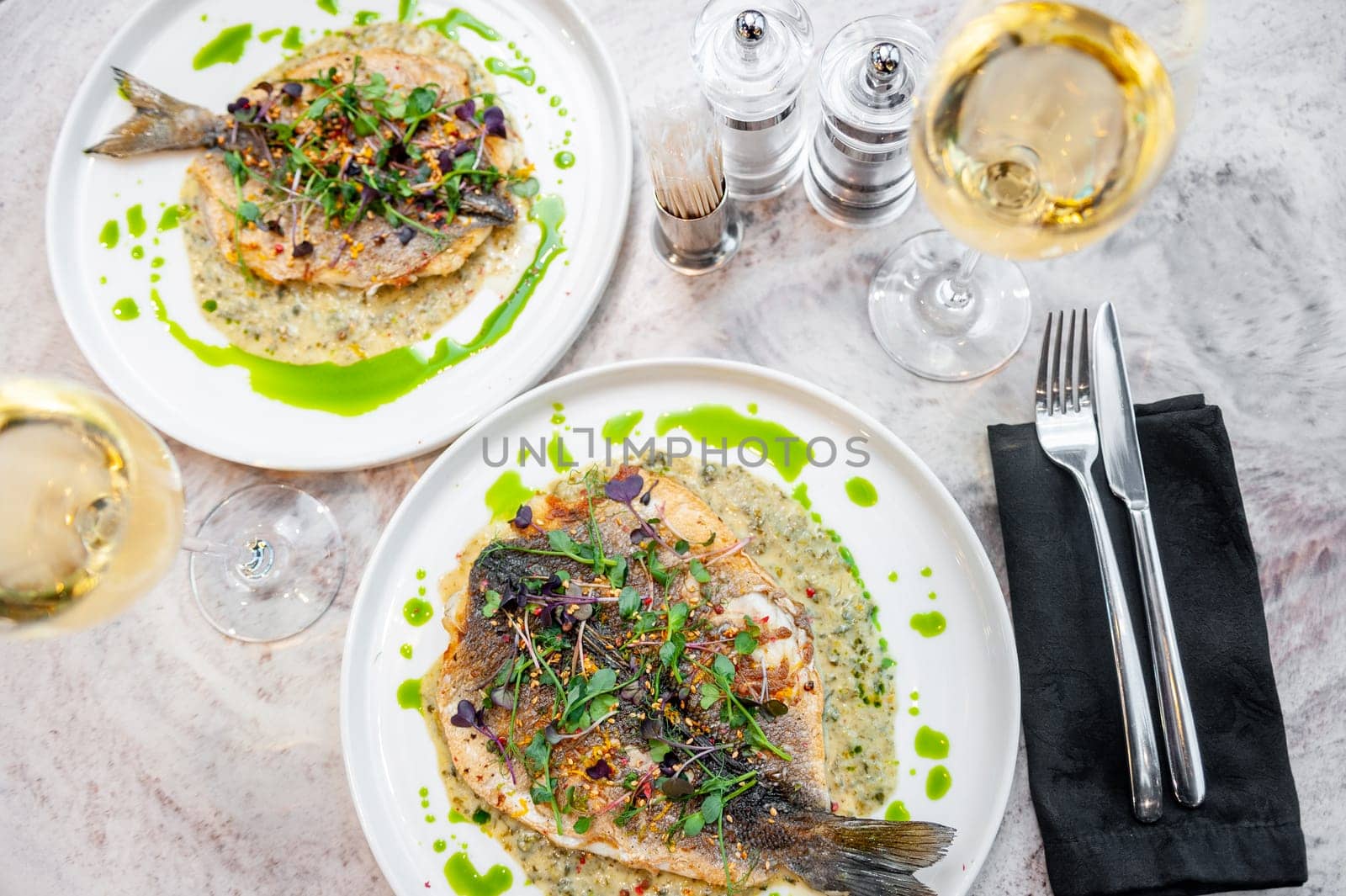 Sea bass in cream sauce with Provencal herbs and green olive oil on a white plate on a marble table in a restaurant