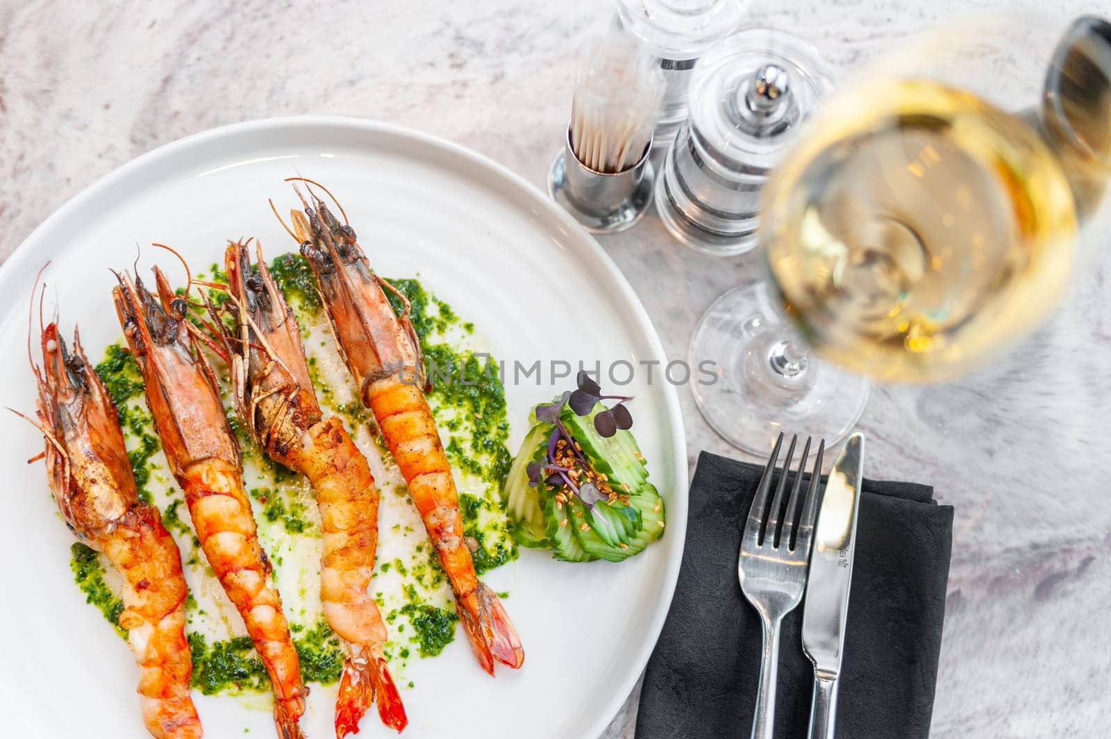 Langoustines with spinach sauce on a white plate on a marble table with a glass of white wine. High quality photo