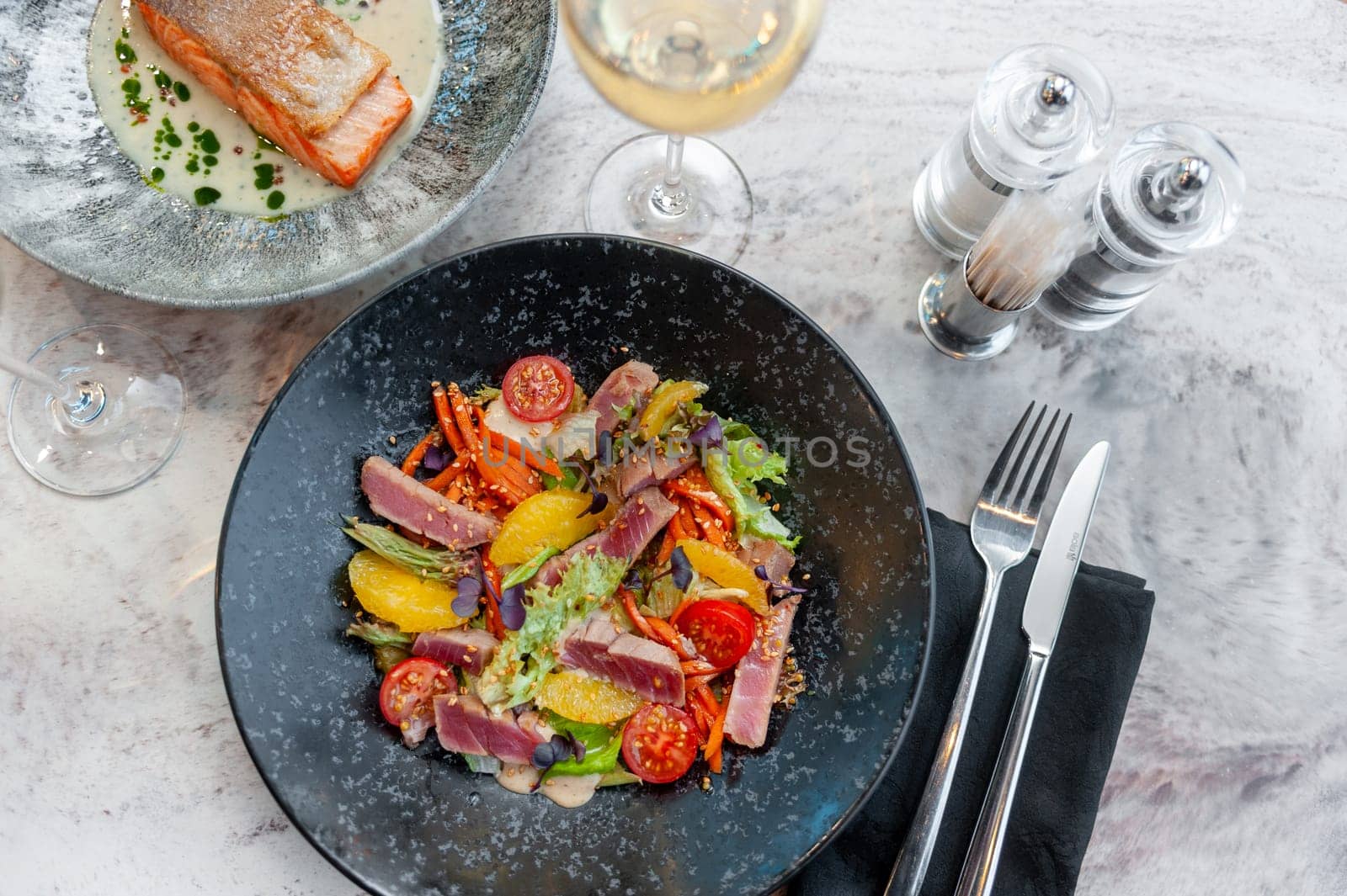 Tuna tataki salad with lettuce, tomatoes and orange on a marble table in a restaurant. High quality photo