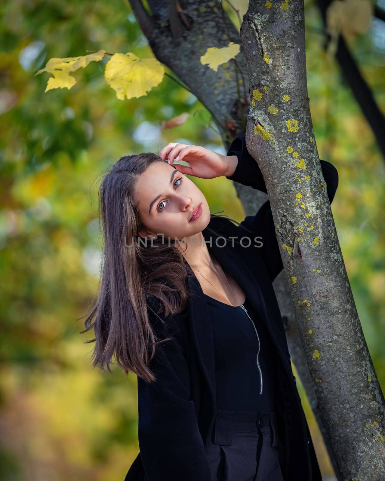 A beautiful girl stands by a tree in an autumn park