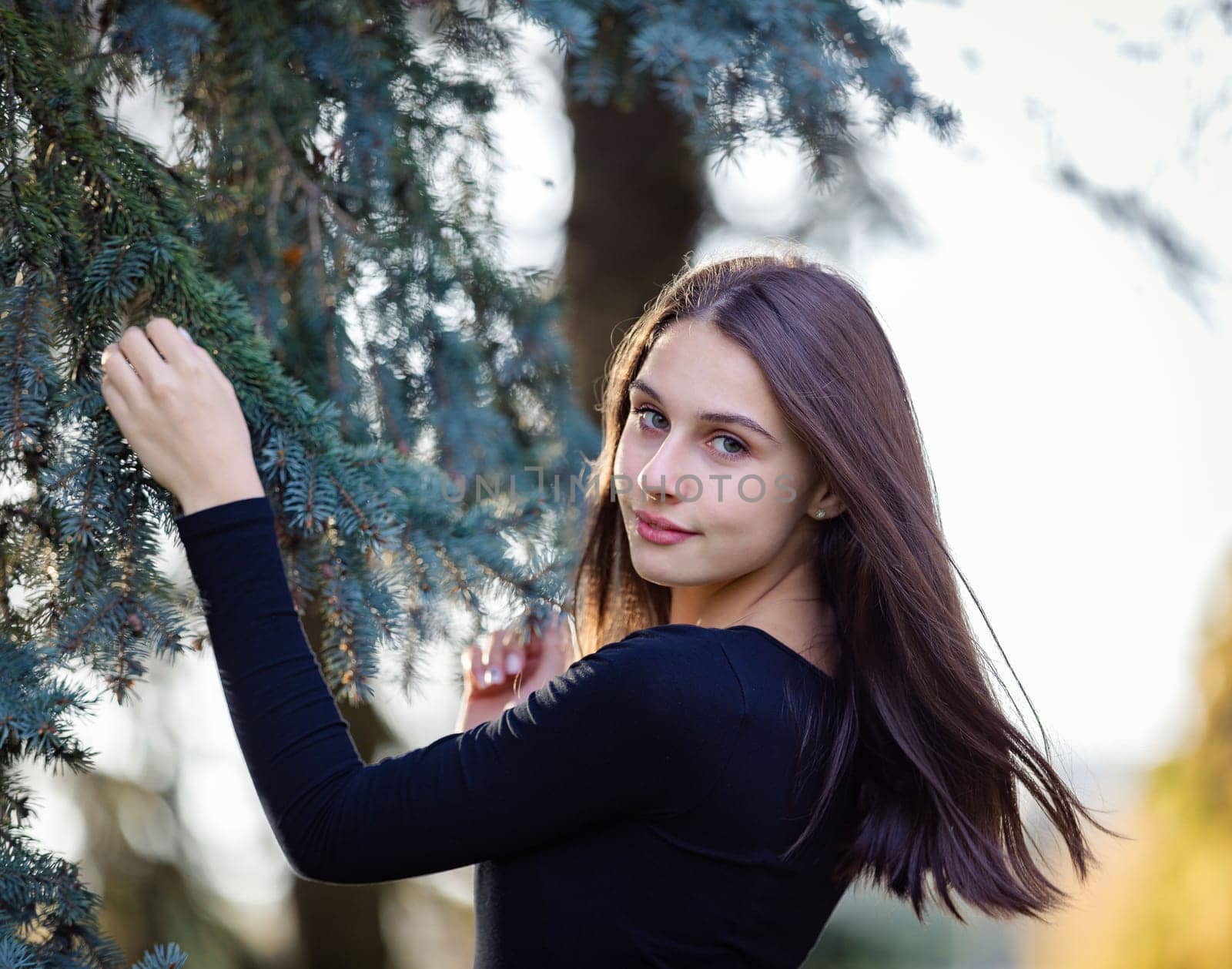 A girl stands near a blue spruce in an autumn park