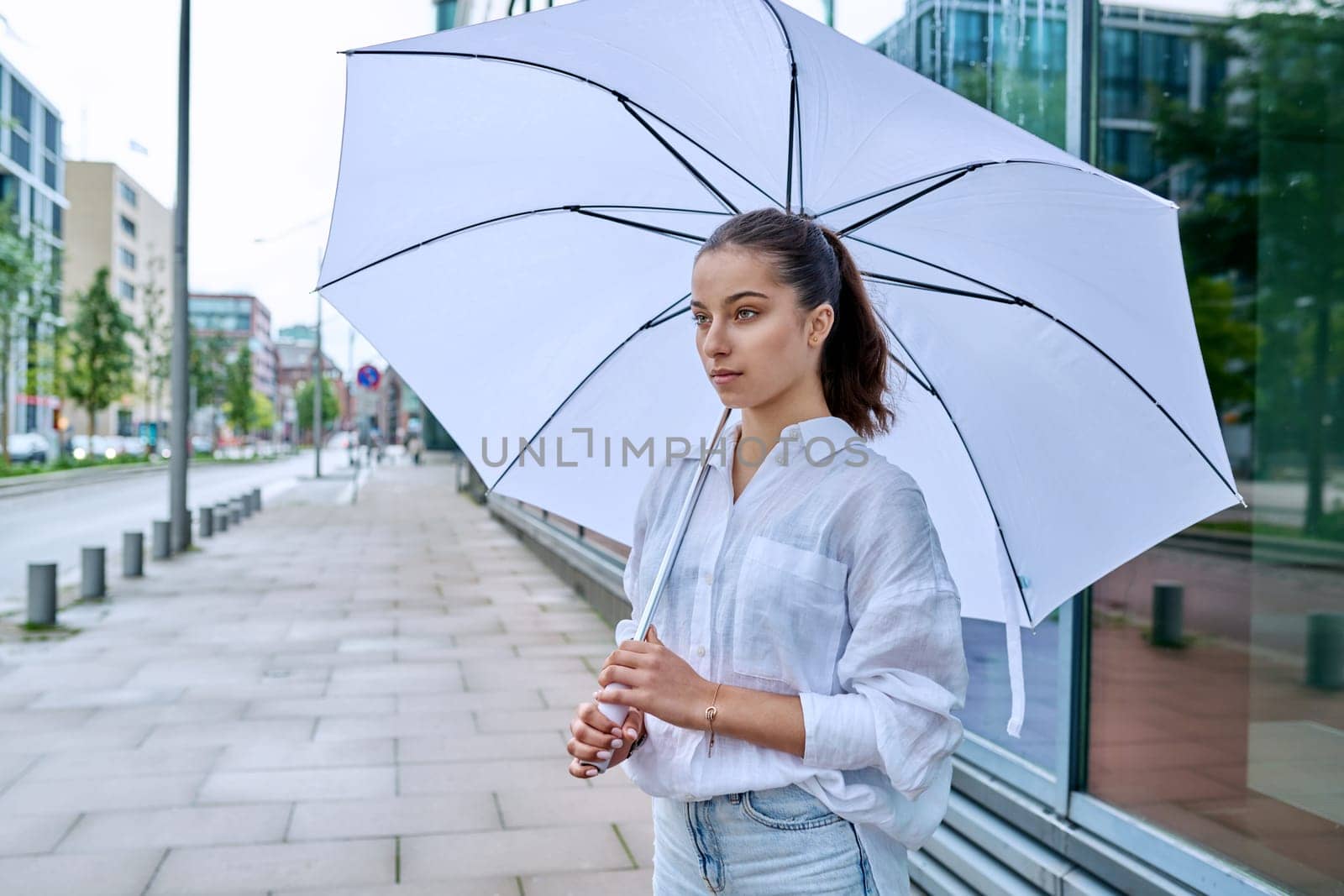 Young teenage female on a summer cloudy day under a white umbrella on a city street