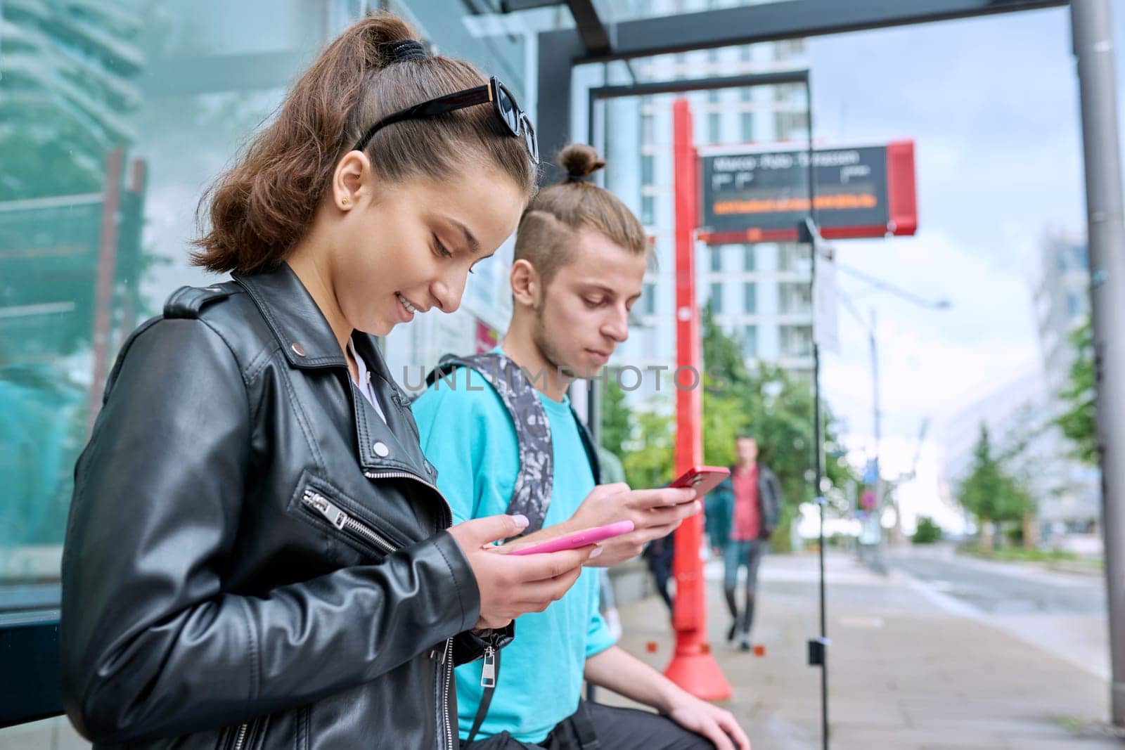 Teenage young people at city bus stop using smartphones by VH-studio