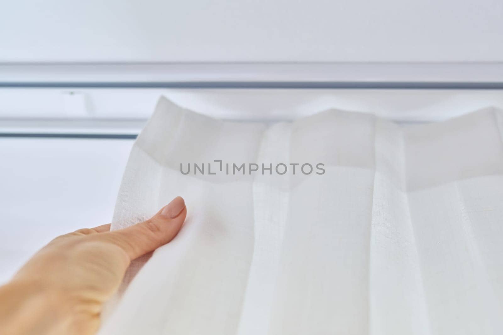 Translucent white textured curtain on window, close-up of ceiling cornice and fabric gathered on braid, laid and sewn with decorative folds, on plastic hooks