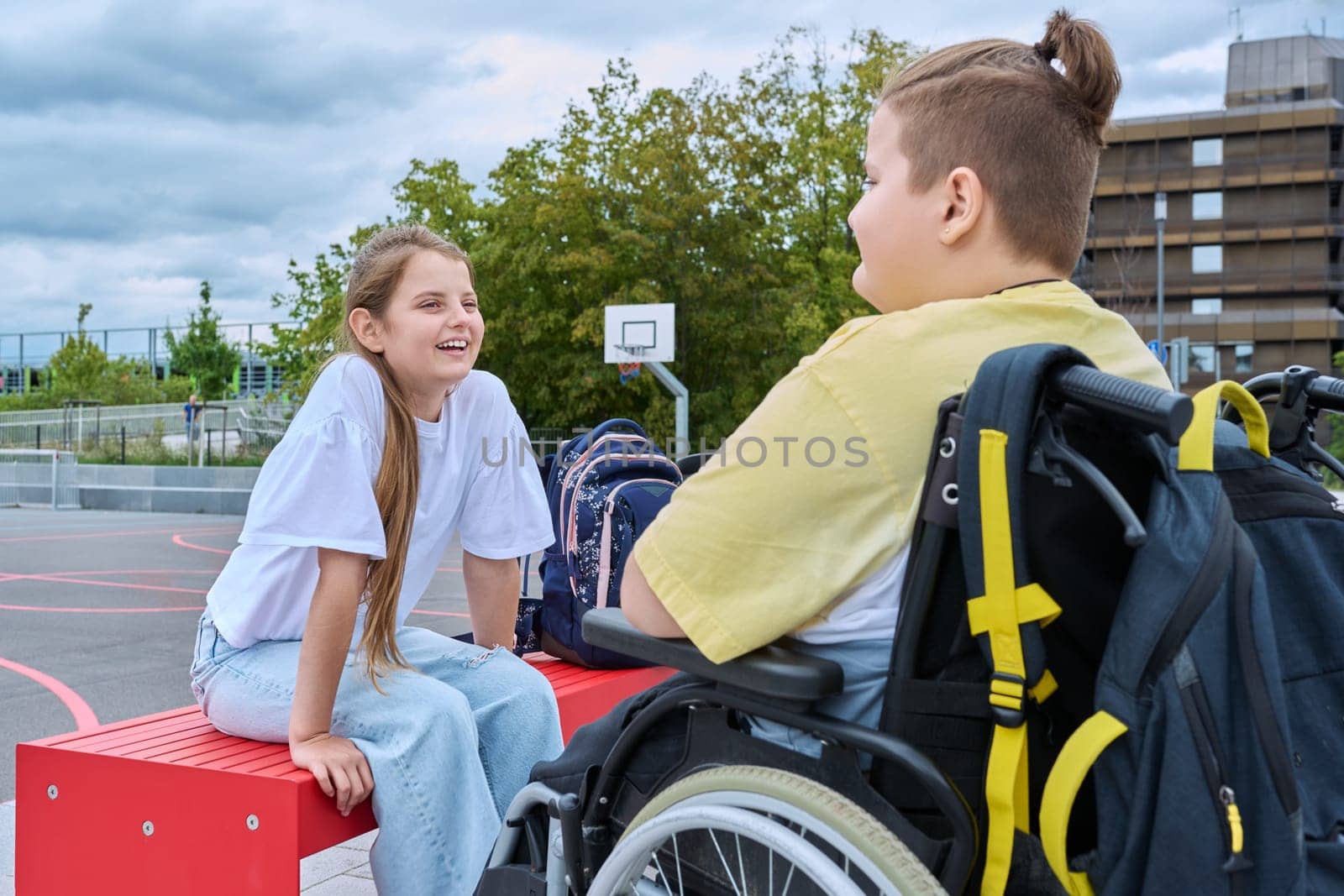Friendship communication of children of boy in wheelchair and girl. Classmates sitting talking after school lessons. Education, disability, inclusiveness concept