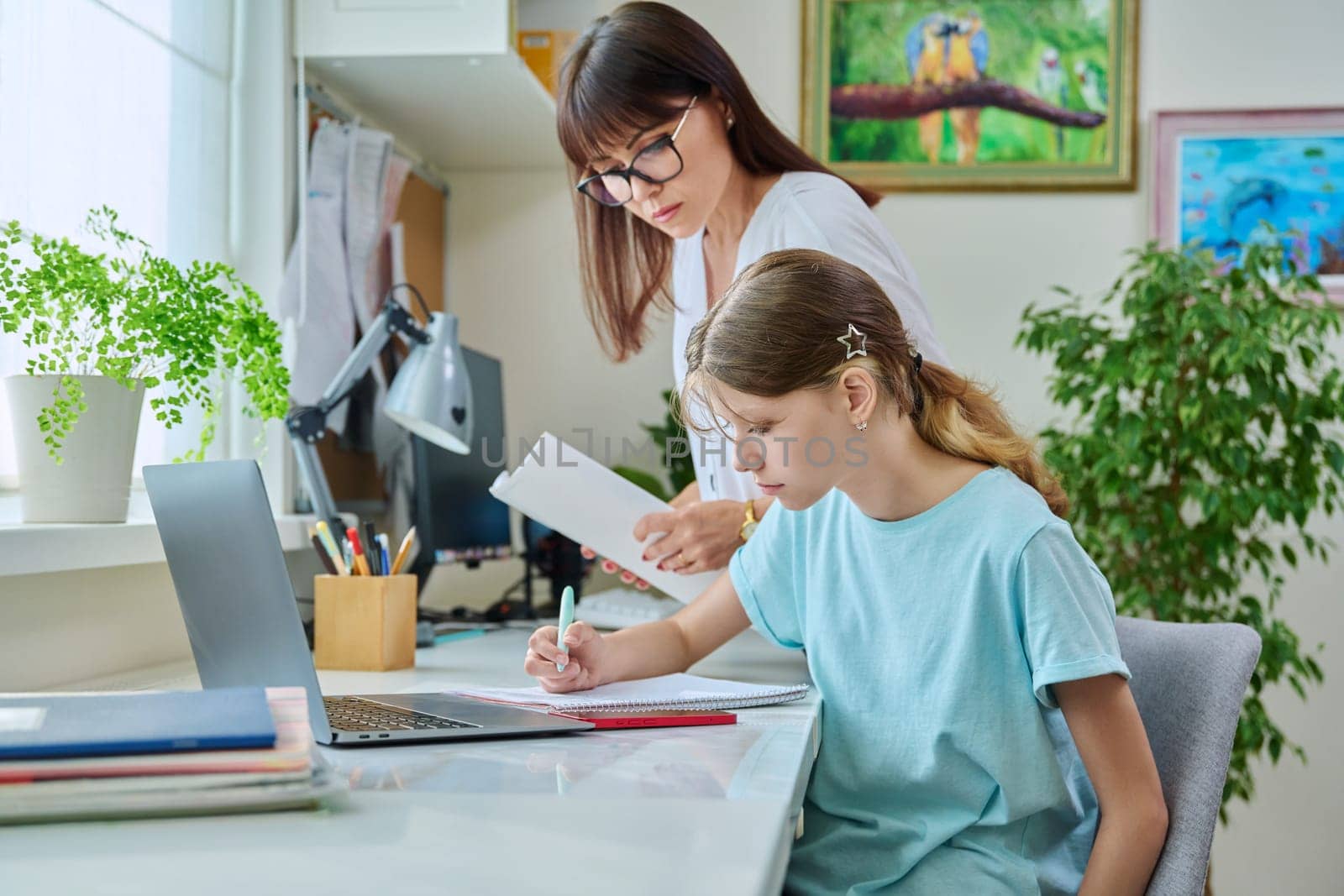 Mother helping preteen daughter to study, looking at laptop at home by VH-studio