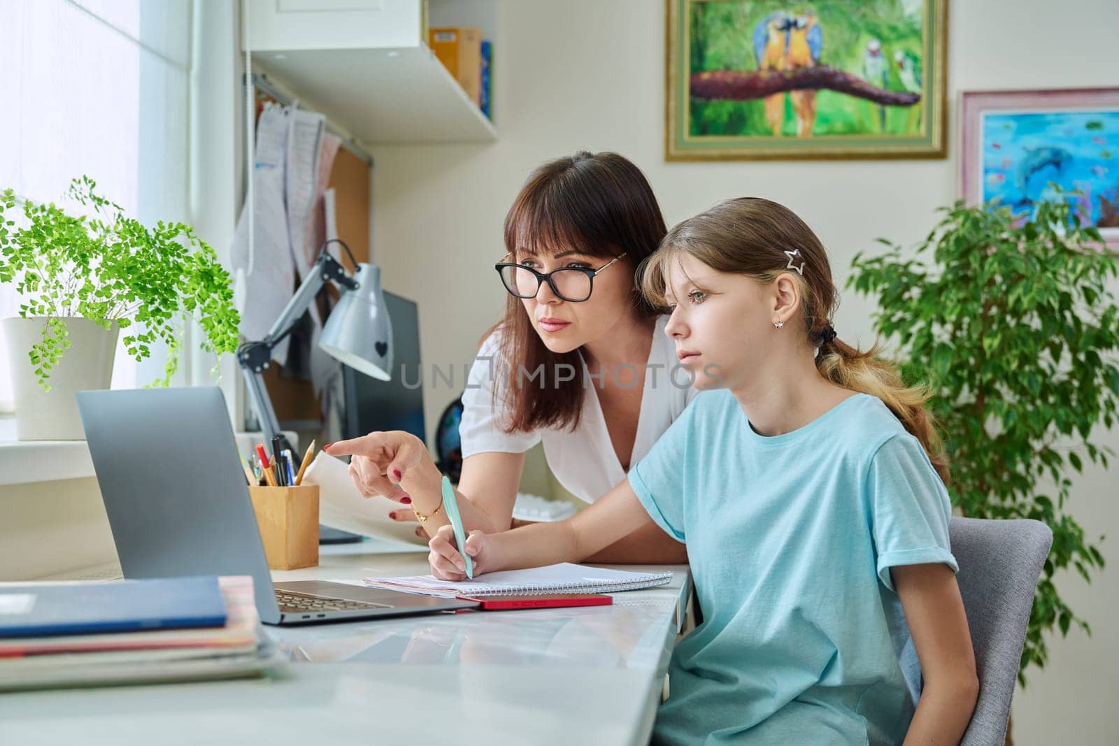 Mother helping preteen daughter to study, looking at laptop computer at desk together at home. Family, home lifestyle, school, education, study, kids concept