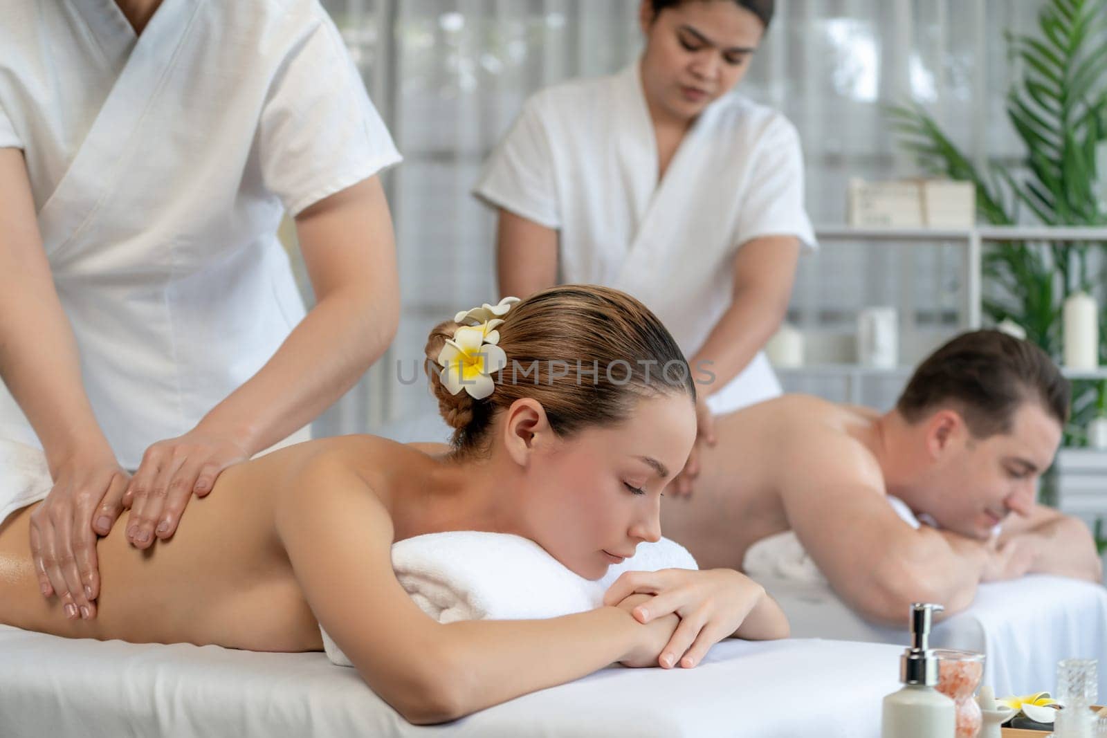 Caucasian couple customer enjoying relaxing anti-stress spa massage and pampering with beauty skin recreation leisure in day light ambient salon spa at luxury resort or hotel. Quiescent