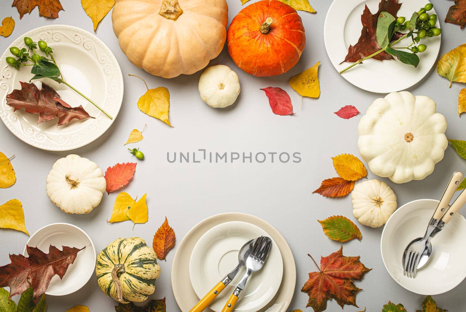 Thanksgiving festive table composition with different colourful pumpkins, autumn leaves, empty plates with cutlery on light grey background table ready for party and celebration. Space for text..