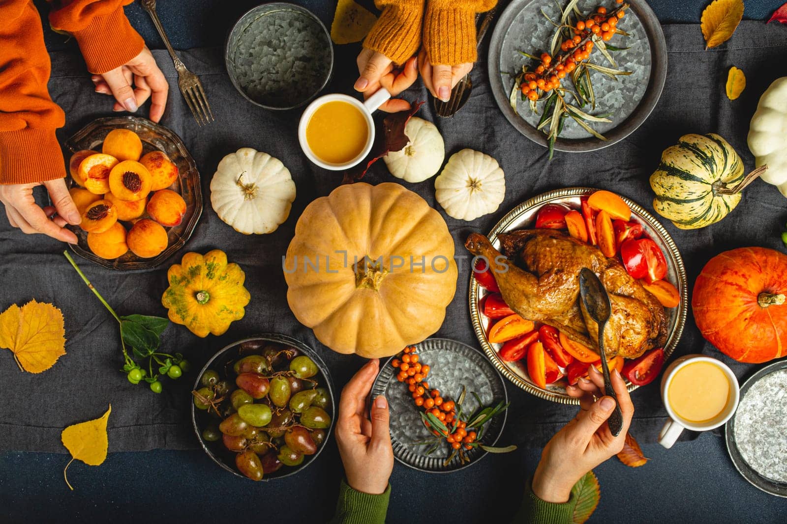 Thanksgiving festive table composition, friends or family eating together roasted turkey, vegetable salad, fruit, orange beverage. Celebration dinner, traditional autumn meals on rustic dark table.