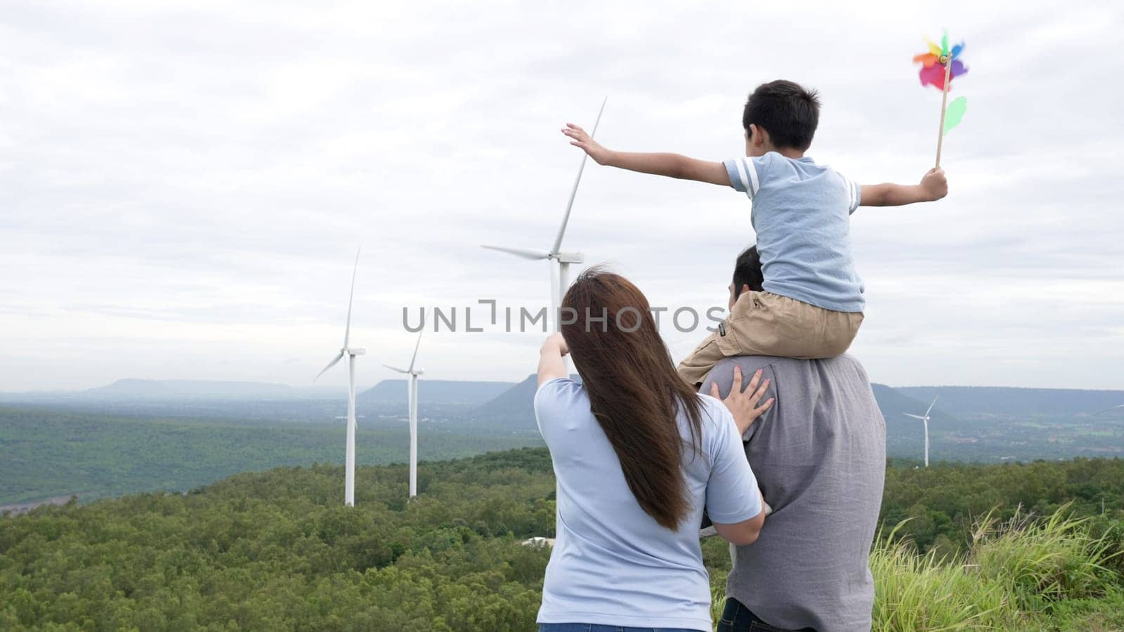 Concept of progressive happy family enjoying their time at the wind turbine farm. Electric generator from wind by wind turbine generator on the country side with hill and mountain on the horizon.