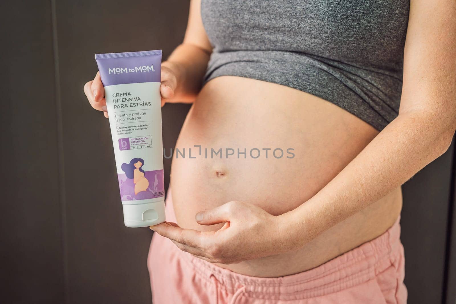 Mexico, Cancun, 02.02.2022: Mom to mom cream for stretch marks for pregnant women. Positive young pregnant woman in comfortable homewear applying belly butter on her big tummy, woman belly by galitskaya