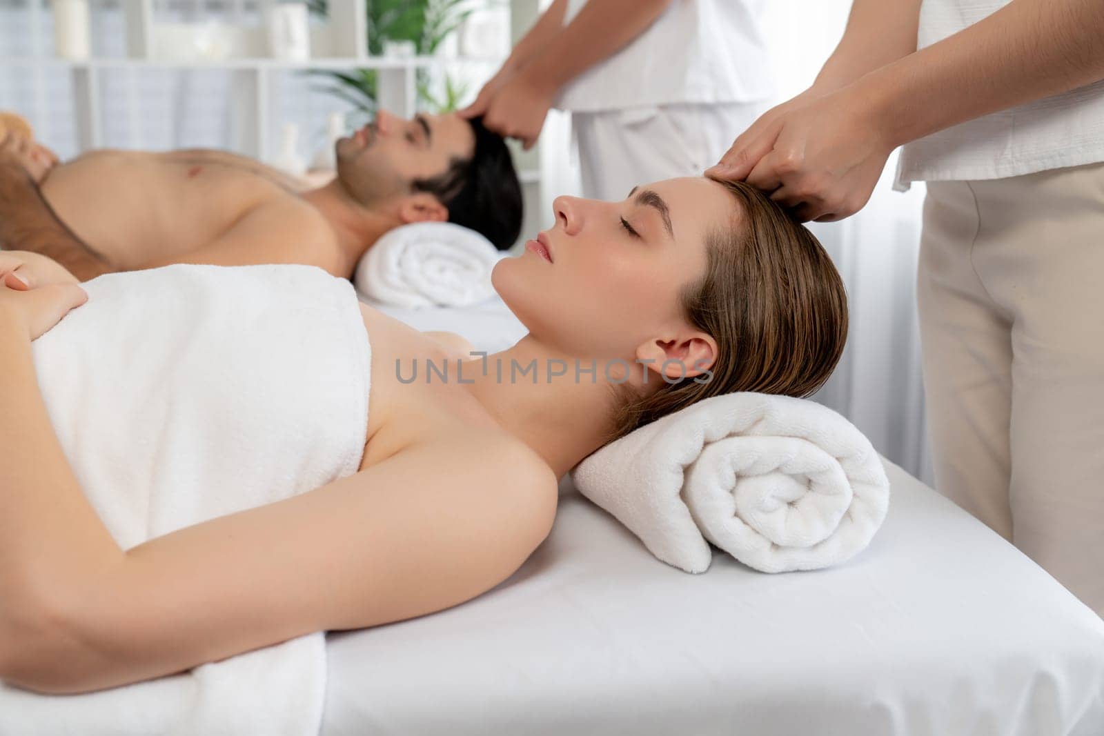 Caucasian couple enjoying relaxing anti-stress head massage and pampering facial beauty skin recreation leisure in dayspa modern light ambient at luxury resort or hotel spa salon. Quiescent