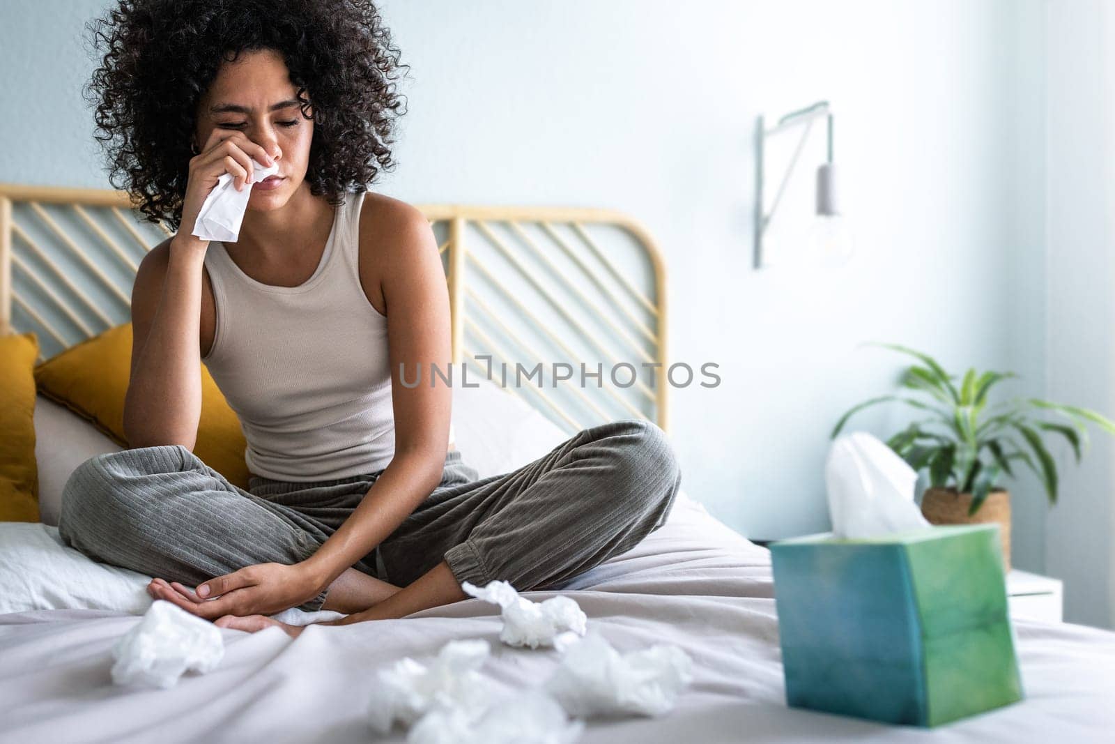 Young multiracial latina woman suffering from a cold, blowing nose with paper tissue. Cold and sickness by Hoverstock