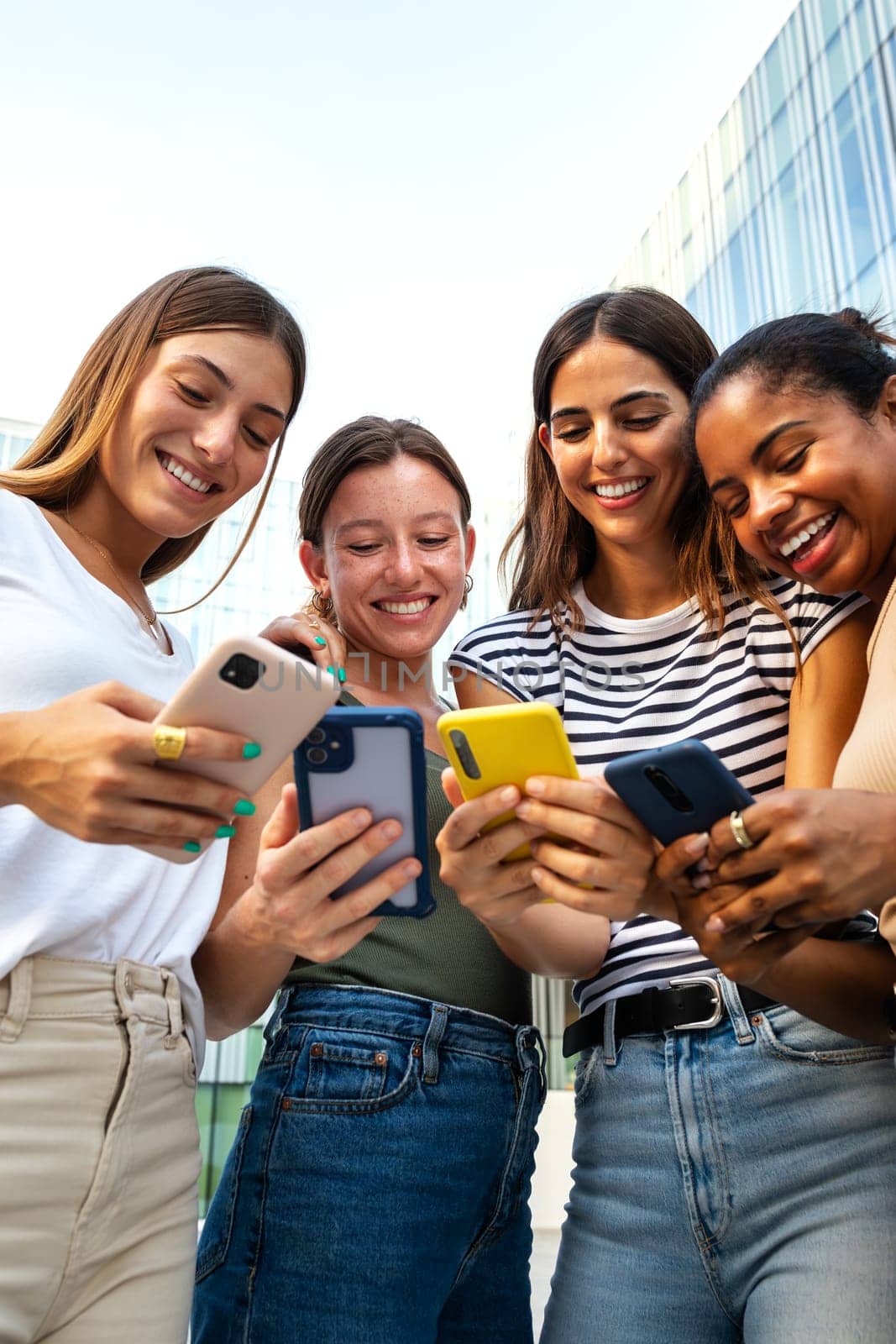 Vertical portrait of happy multiracial group of young women friends looking at mobile phone. by Hoverstock